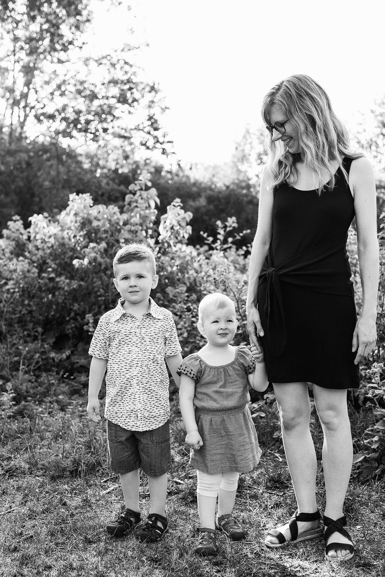 Black and white photo of small children walking with parent through a garden path.