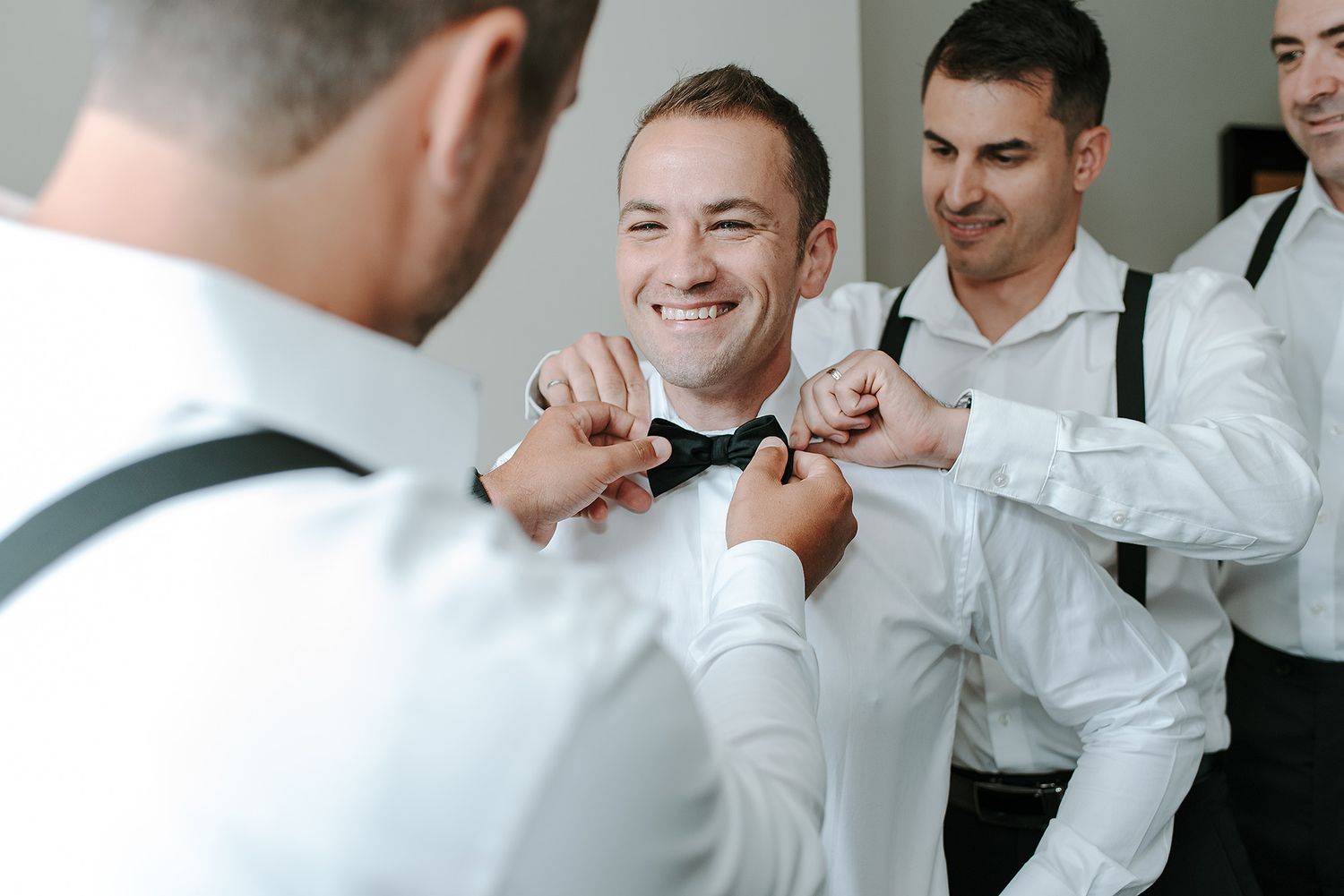 Groomsmen in white dress shirts help each other get ready before a wedding ceremony.