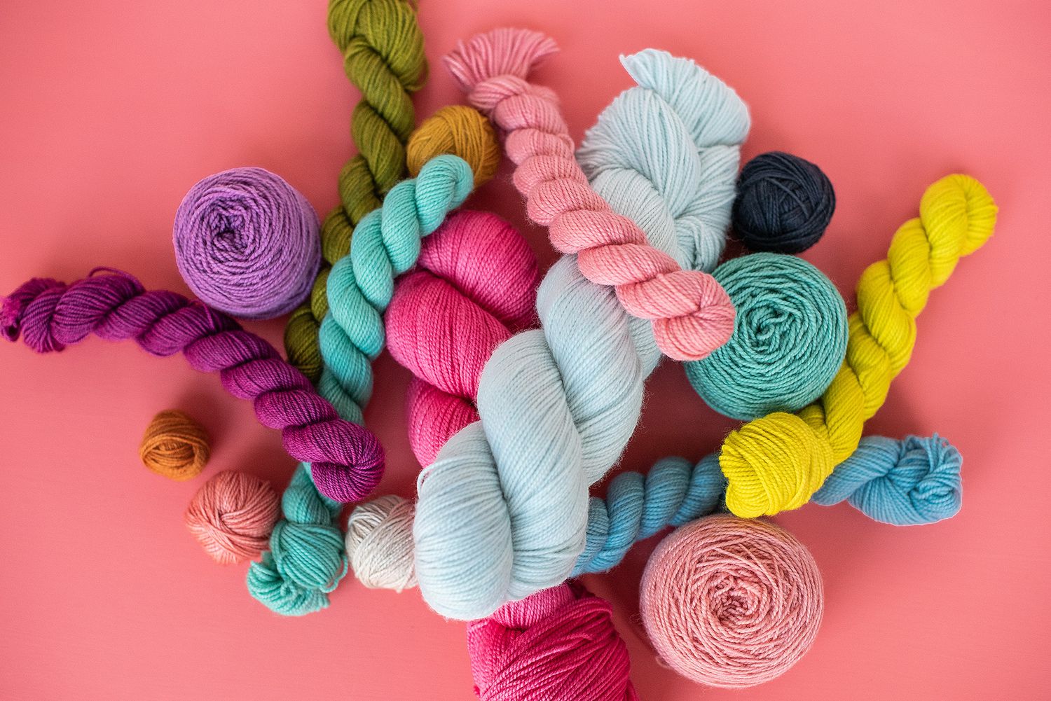 Collection of vibrant yarn balls arranged in a row against a coral pink background.