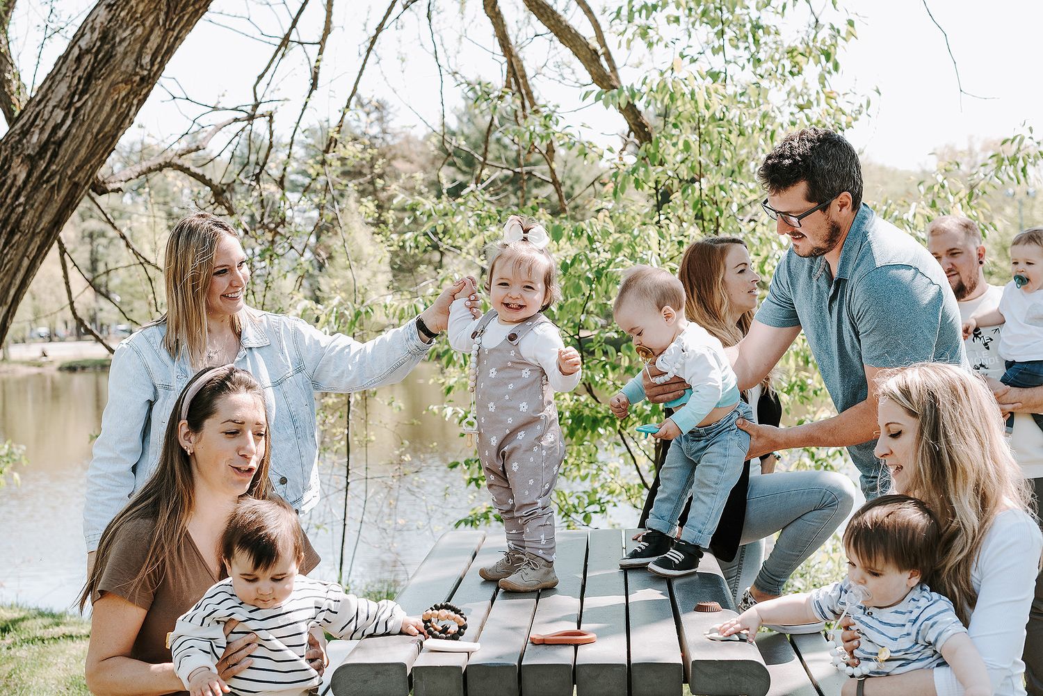 Multiple shots of a family gathering around a picnic table near a lake with trees in the background.