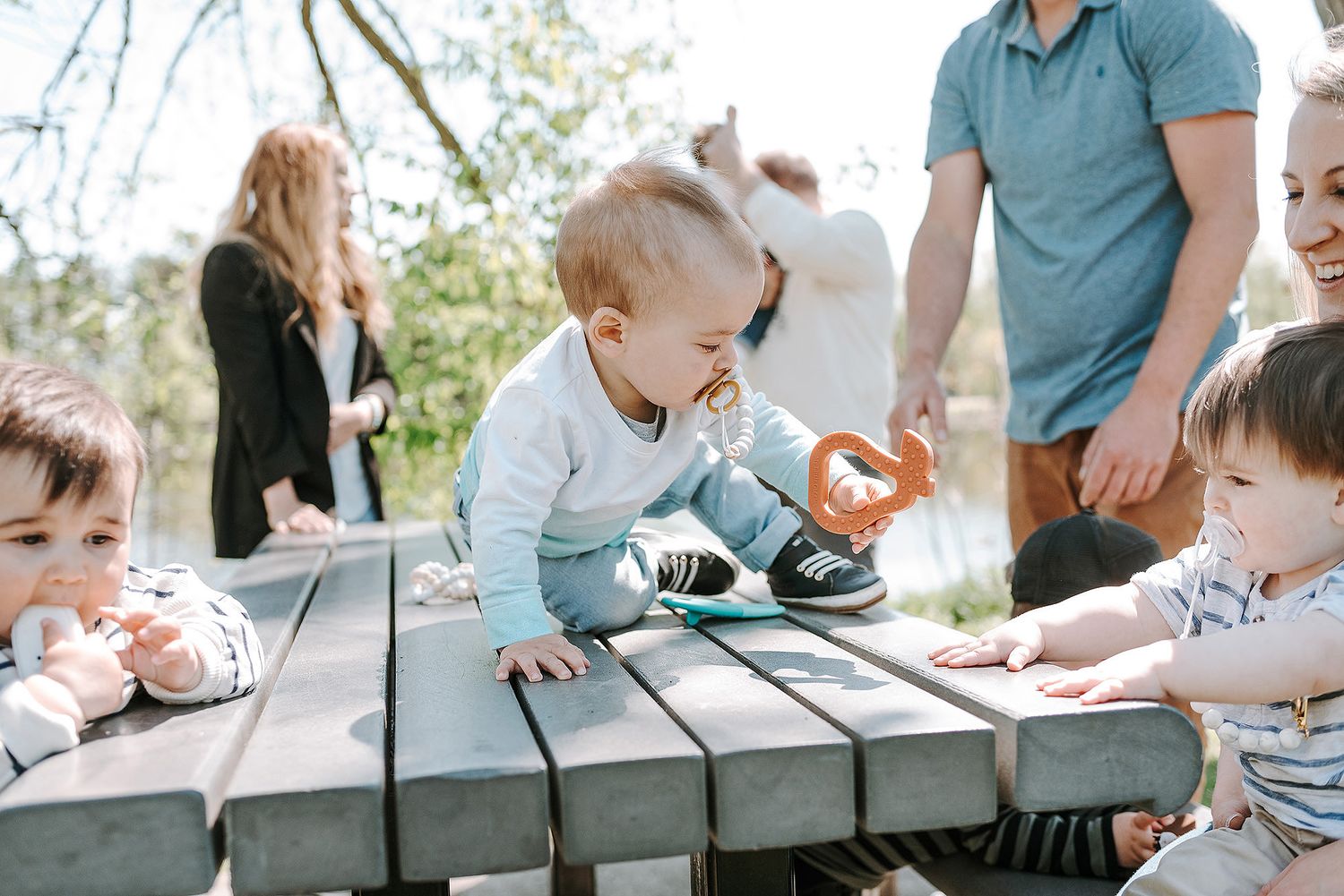 Families gathered around picnic tables for outdoor social event with children.
