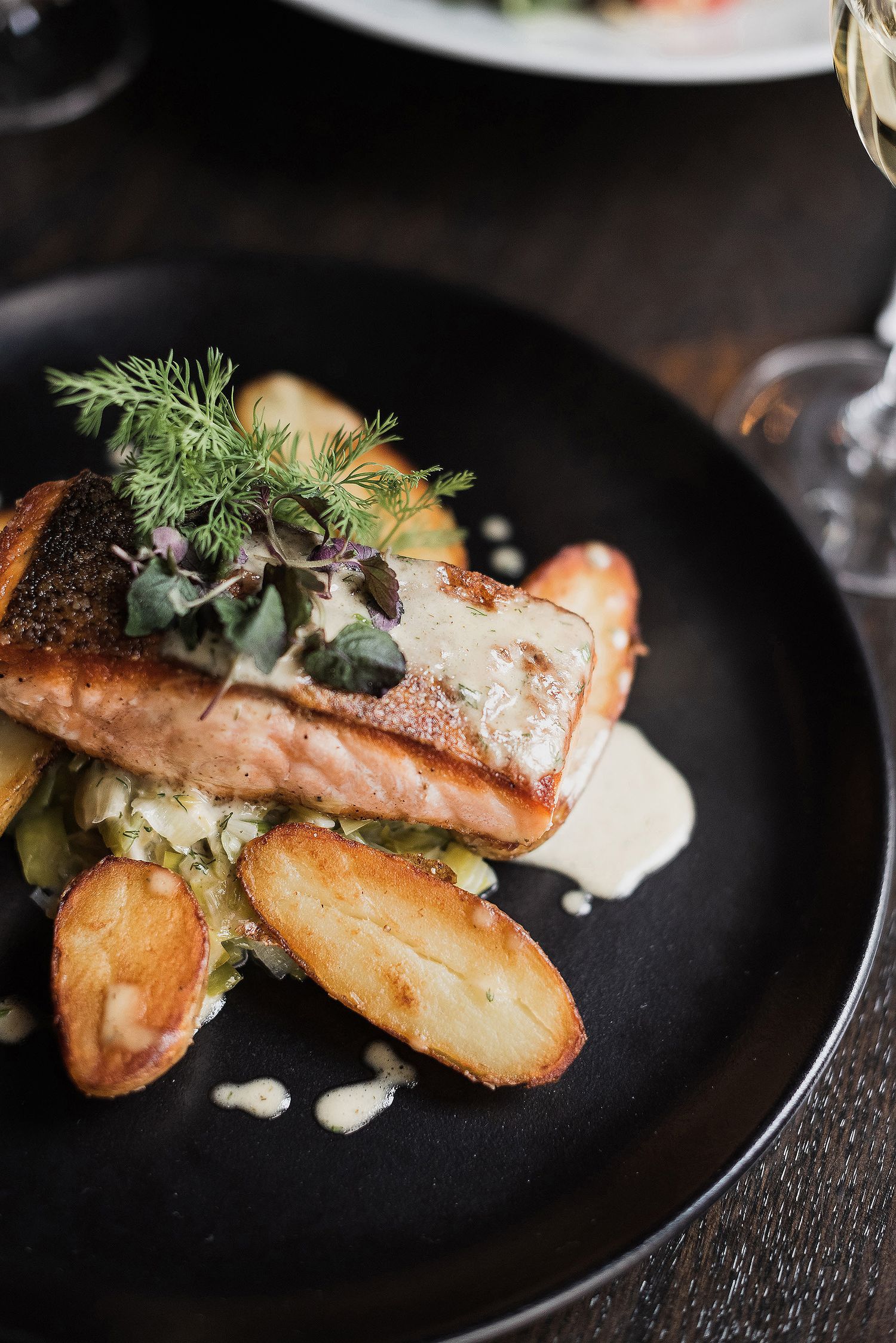 Grilled salmon fillet with creamy sauce and fresh herbs served on black plates in an elegant presentation.