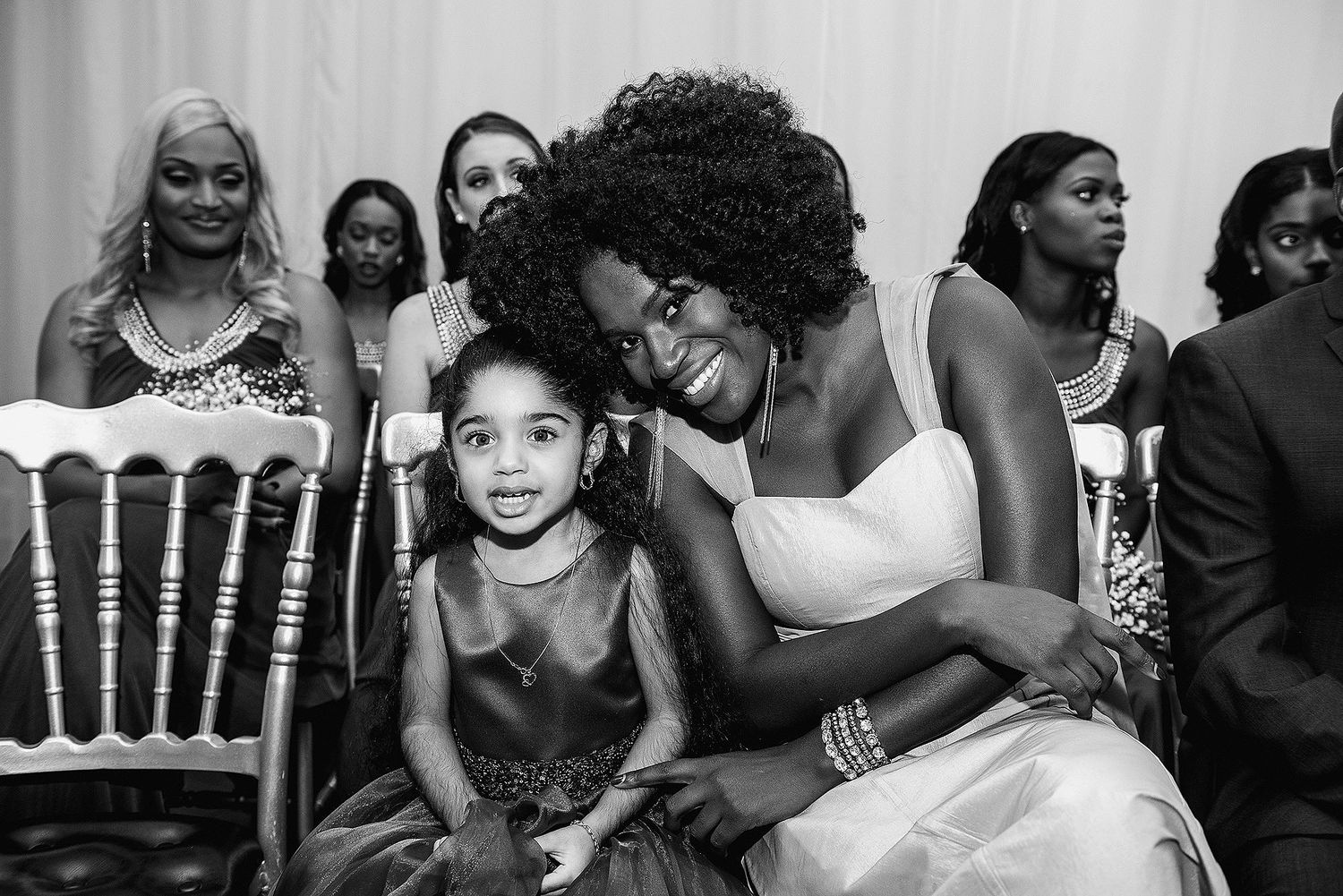 Black and white photo of a woman in a wedding dress hugging a young girl at a formal celebration.