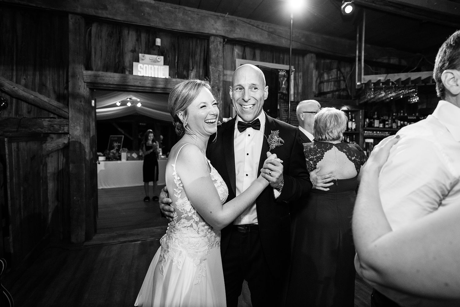 A couple dances together during a wedding reception in a dimly lit venue with spotlights overhead.