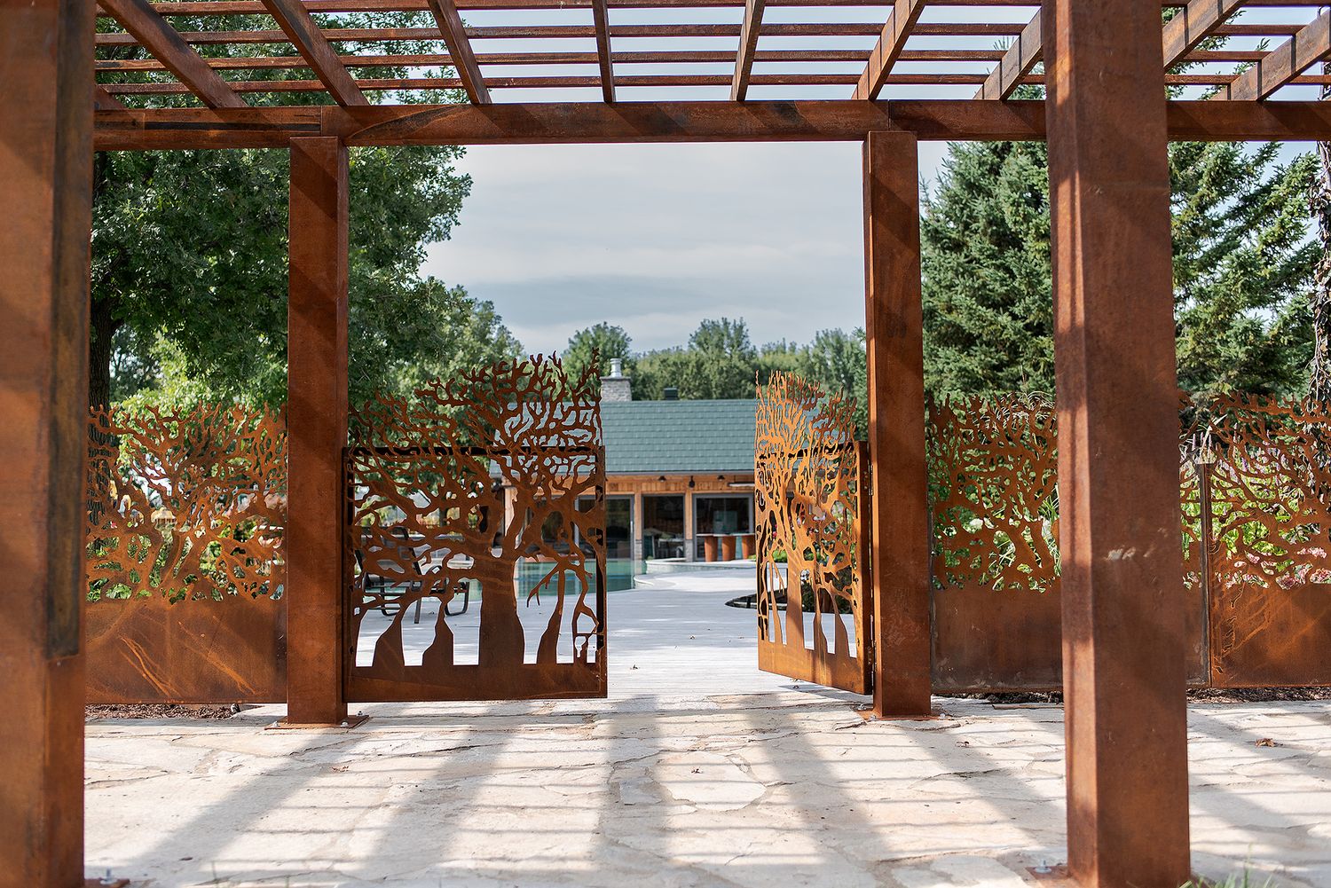 A panoramic view of a wooden pergola walkway with sunlight streaming through slats casting shadows on a garden path.