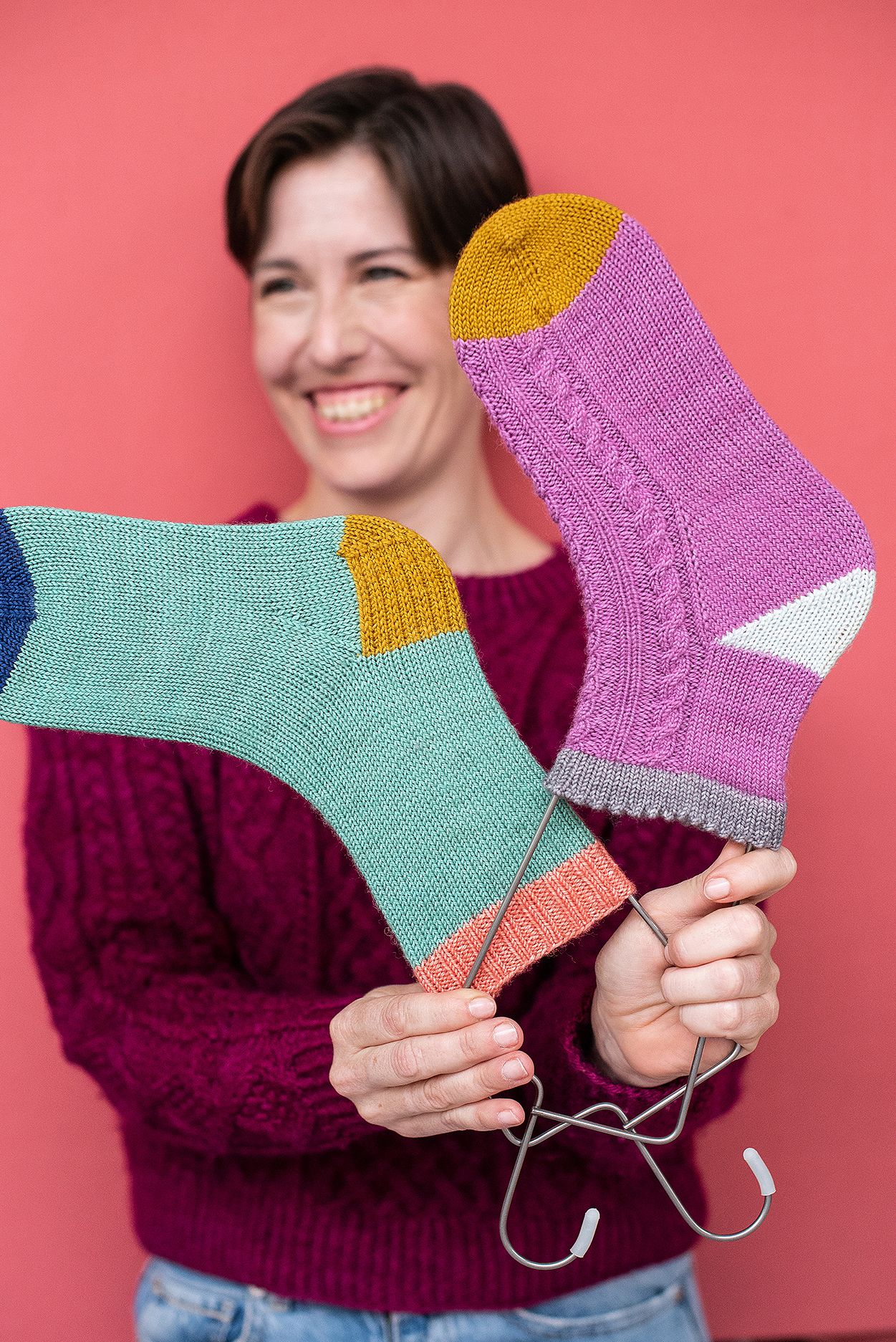 Handmade knitted socks in mint green, purple and mustard colors being displayed against coral background.