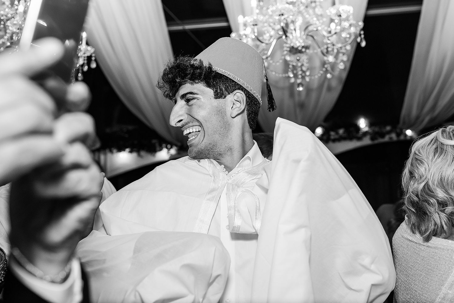 A black and white photo of a joyful wedding celebration with people laughing and dancing at a reception.