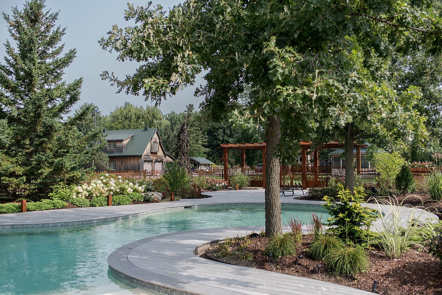 A tranquil backyard oasis features a natural stone swimming pool surrounded by lush landscaping and mature trees.