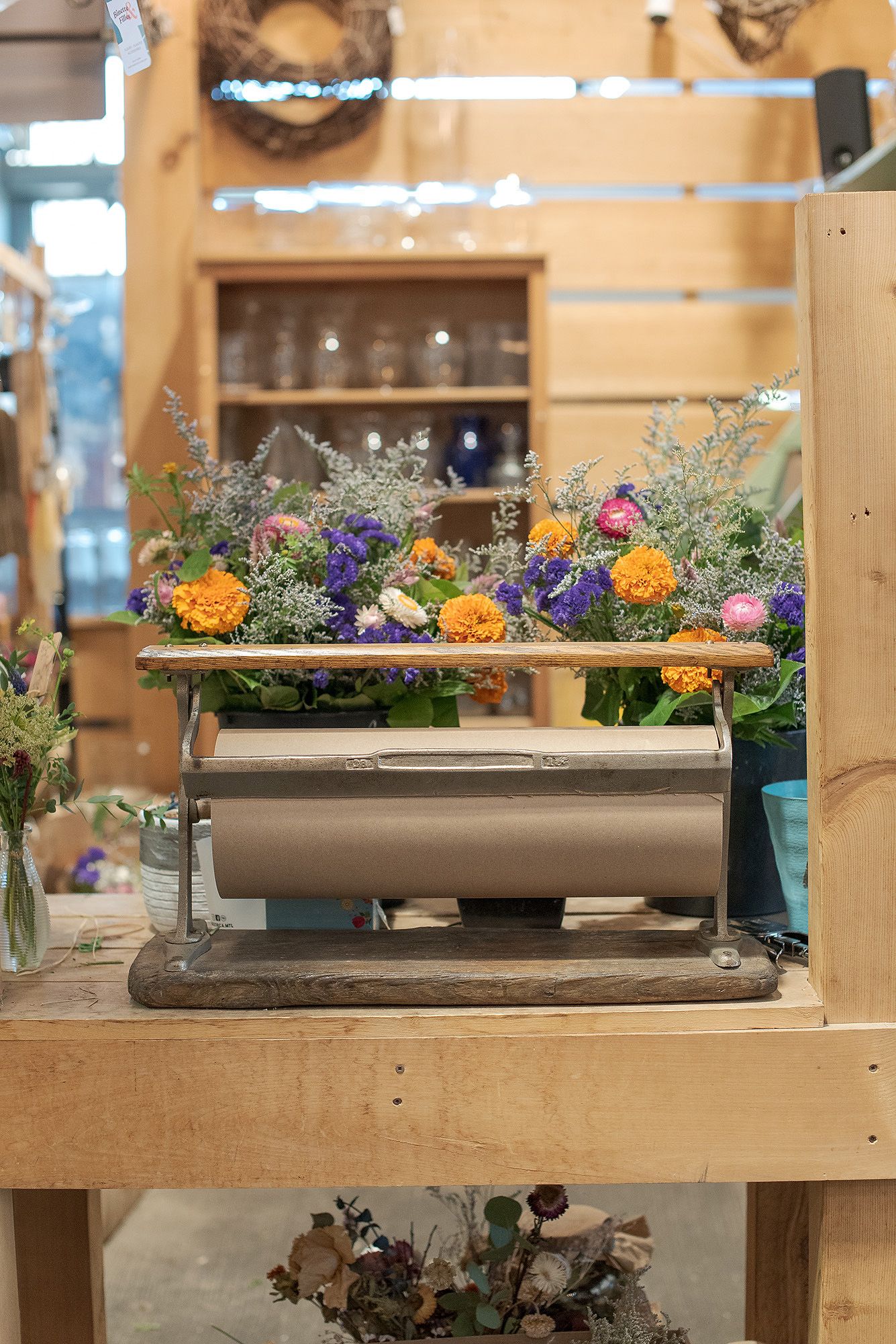 Colorful floral arrangements in brown planter boxes displayed on wooden shelves in a rustic setting.