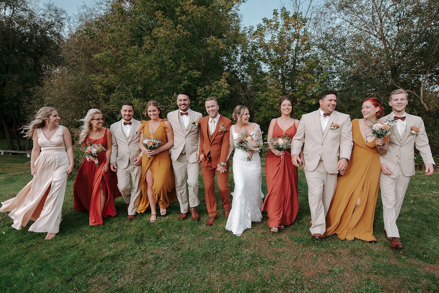 Wedding party in coordinated earth tones and rust colors posed together on grassy hillside.
