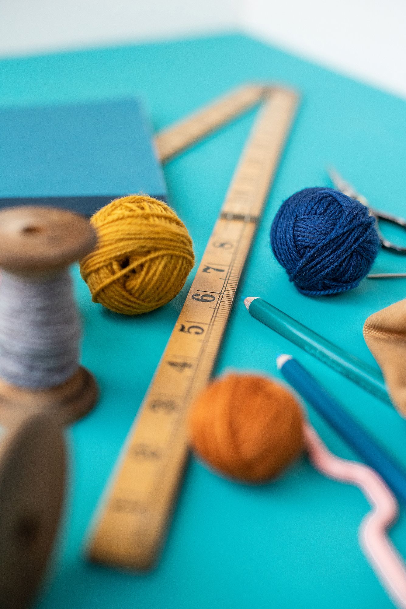 Colorful yarn balls and wooden ruler arranged on turquoise background for knitting project.