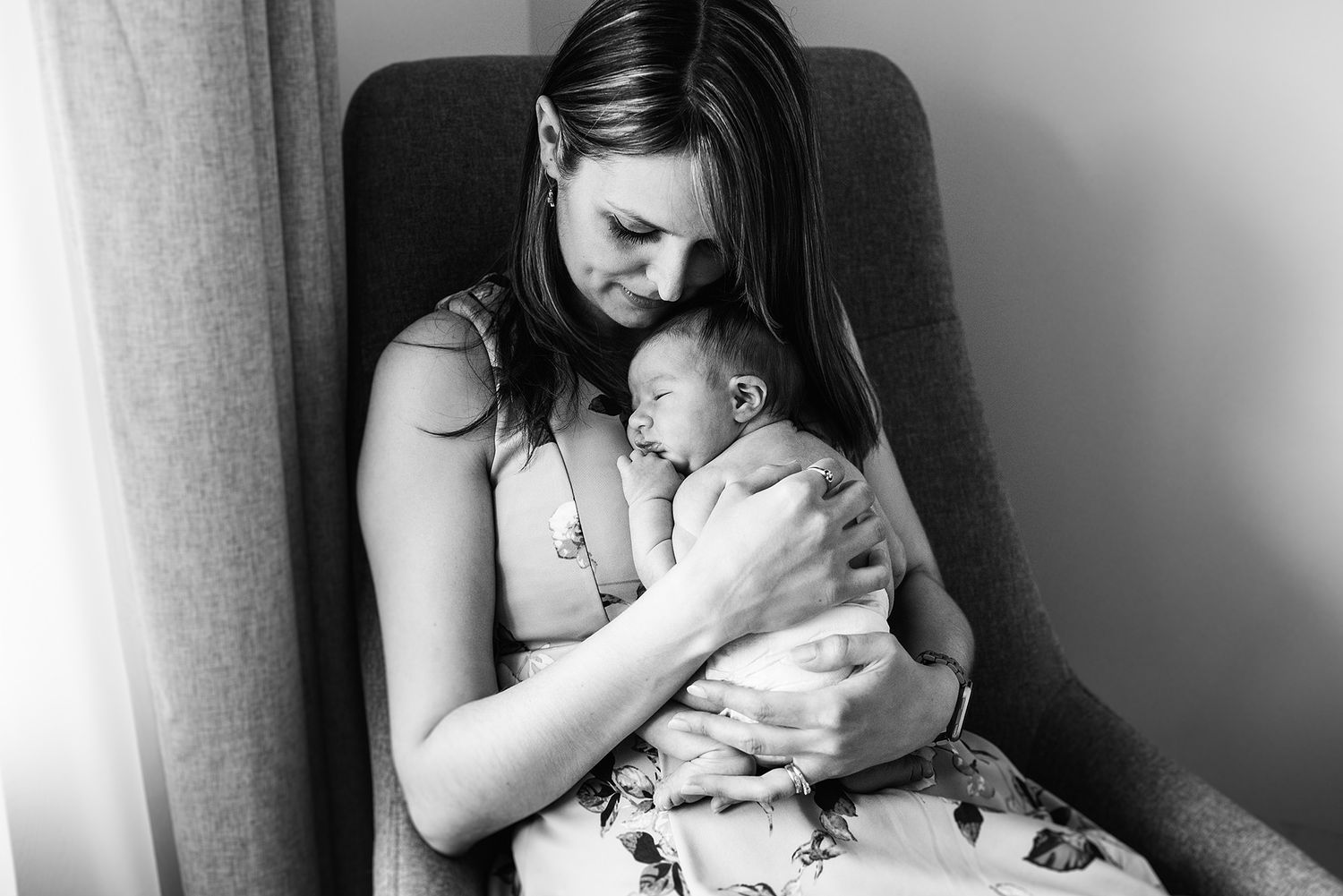 Intimate black and white portrait of parent and baby in soft window light.
