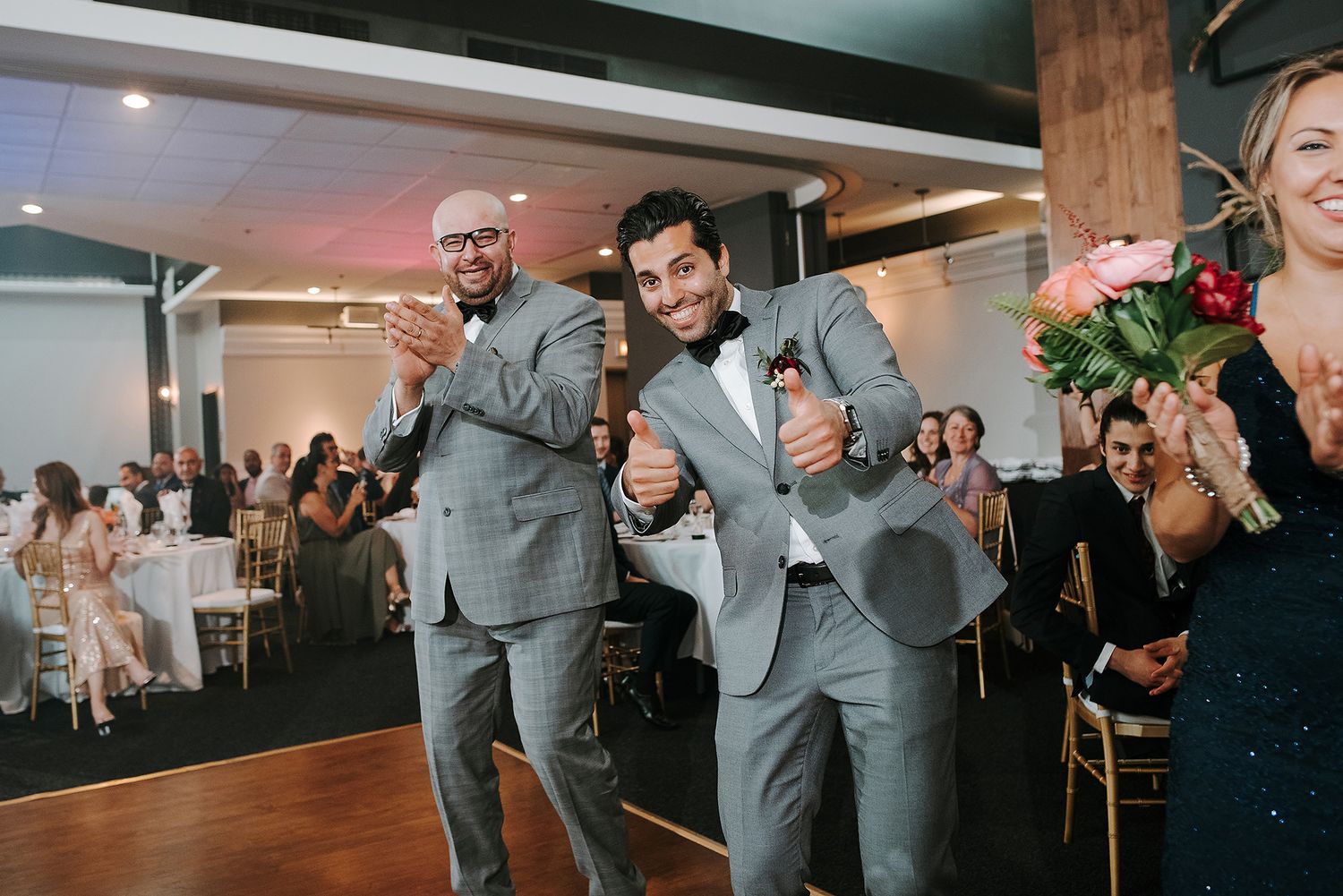 Wedding party members in gray suits dance and celebrate during a reception in an indoor venue.