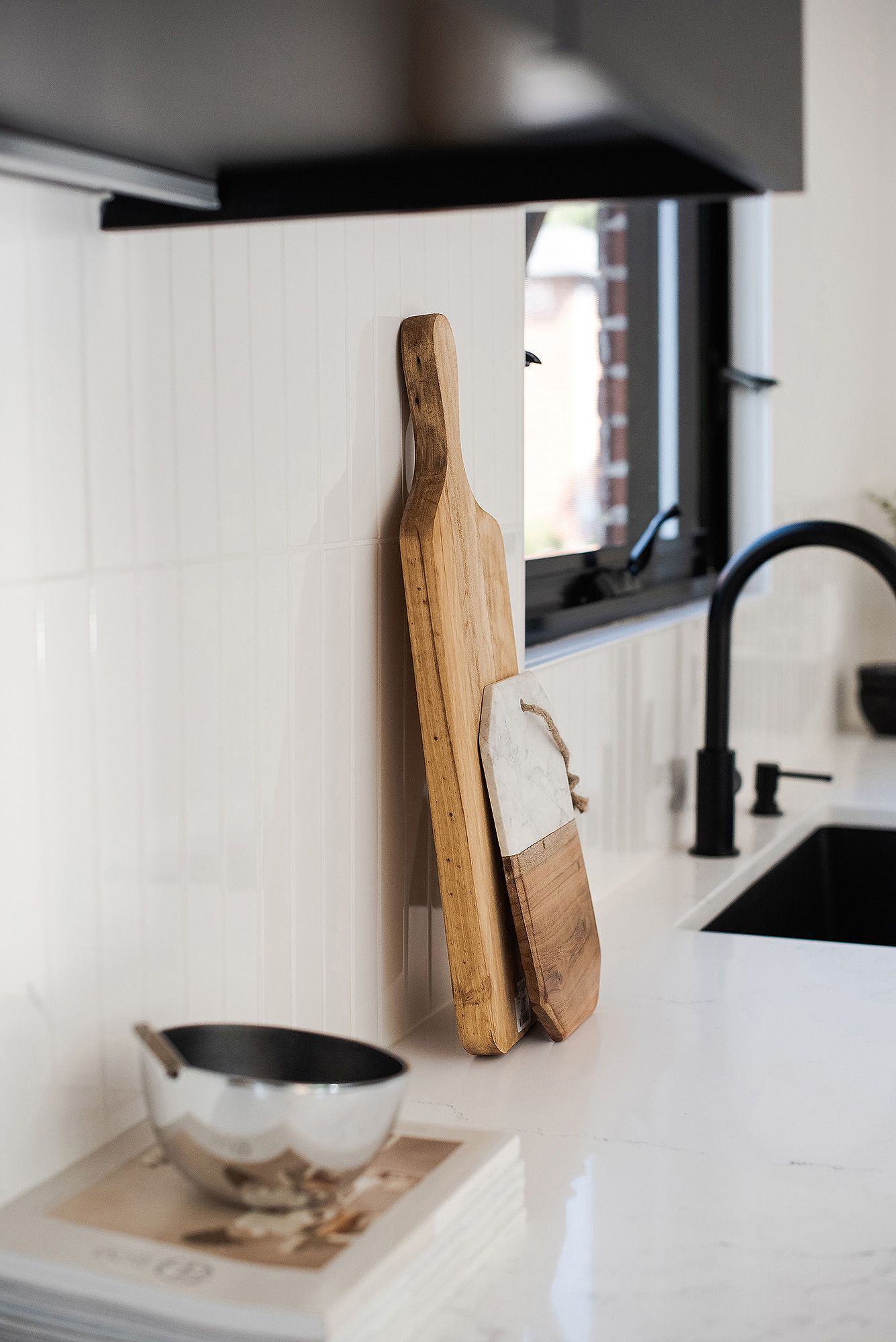 Rustic wooden cutting boards displayed against white wall near black kitchen cabinets.