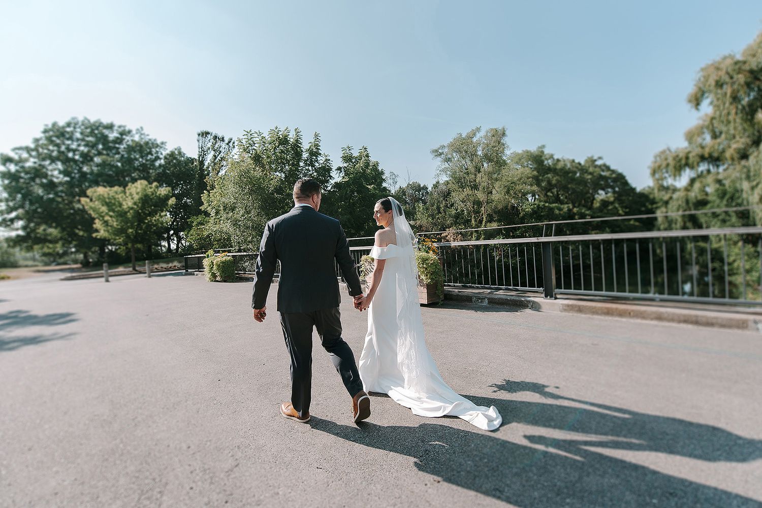 A couple in wedding attire walks together on a scenic path during their outdoor wedding photoshoot.