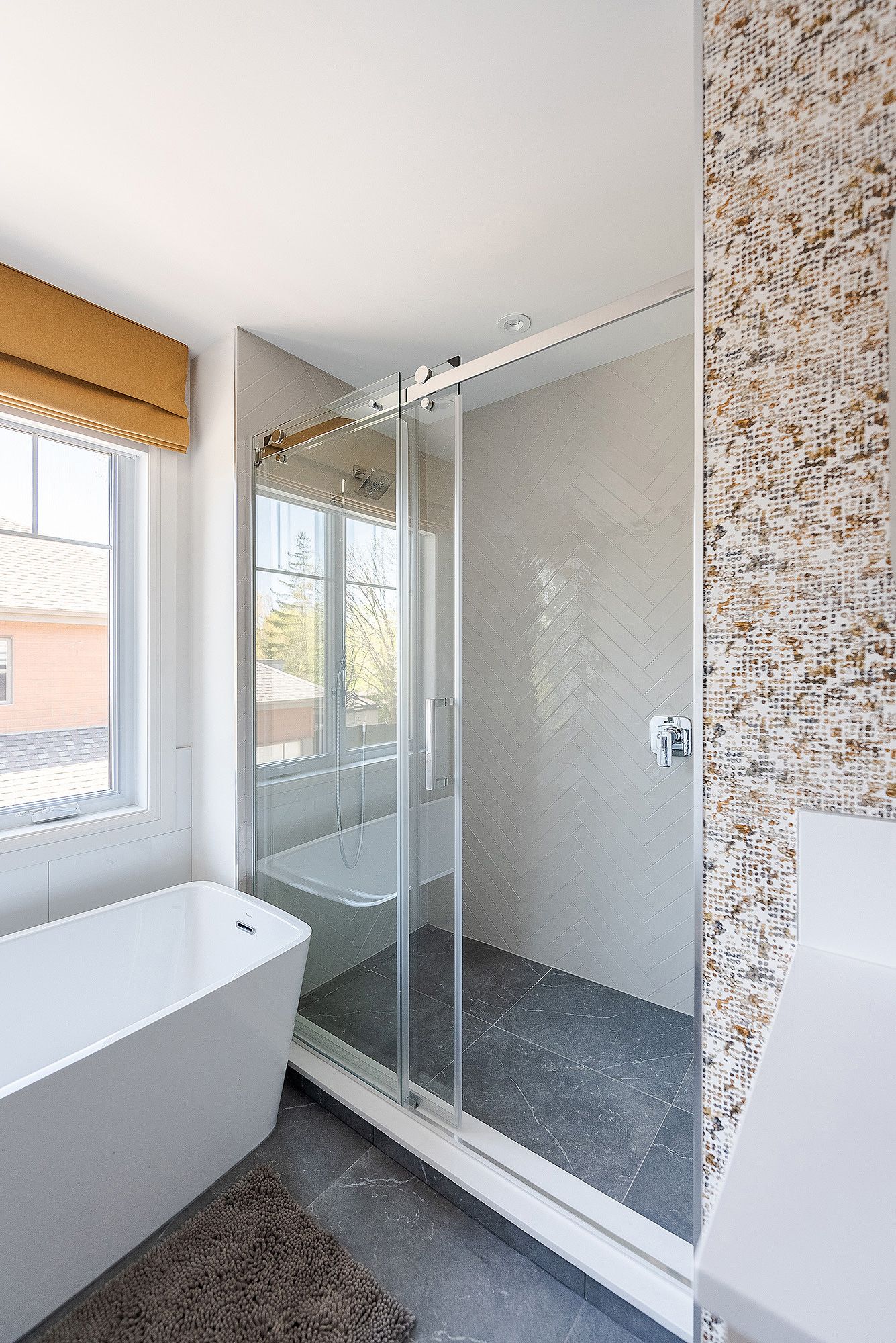 Modern bathroom interior with freestanding bathtub, glass shower enclosure, and textured stone accent wall.