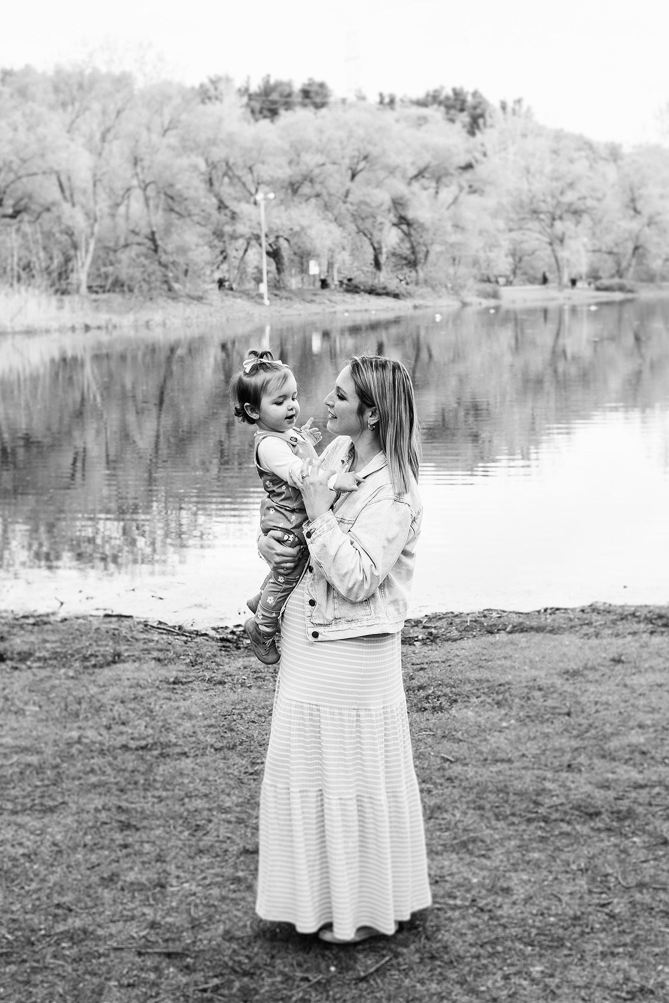 Black and white portrait by a serene lake with trees reflecting in the water.