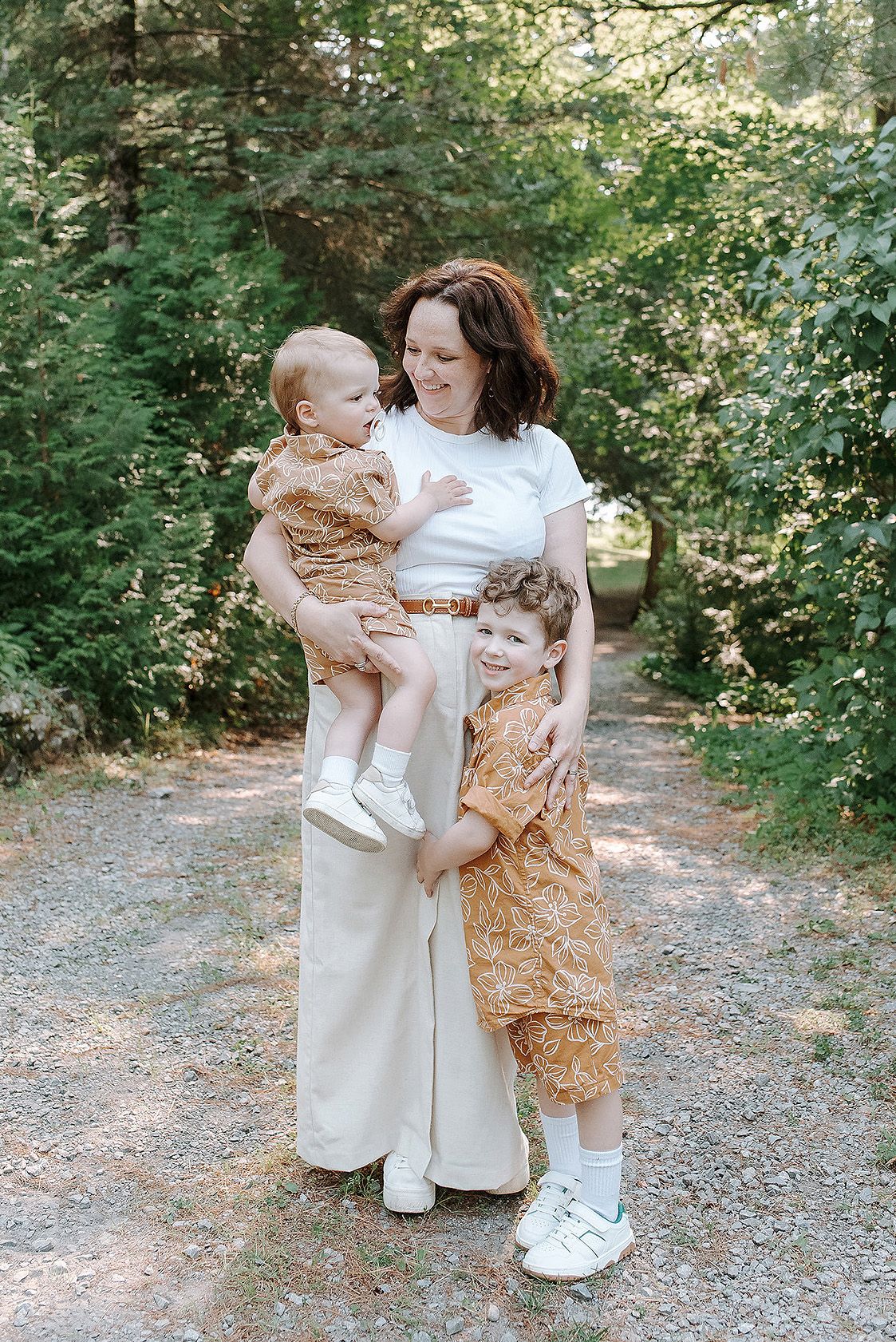 A tender family moment captured in a series of outdoor photos on a wooded path with dappled sunlight.