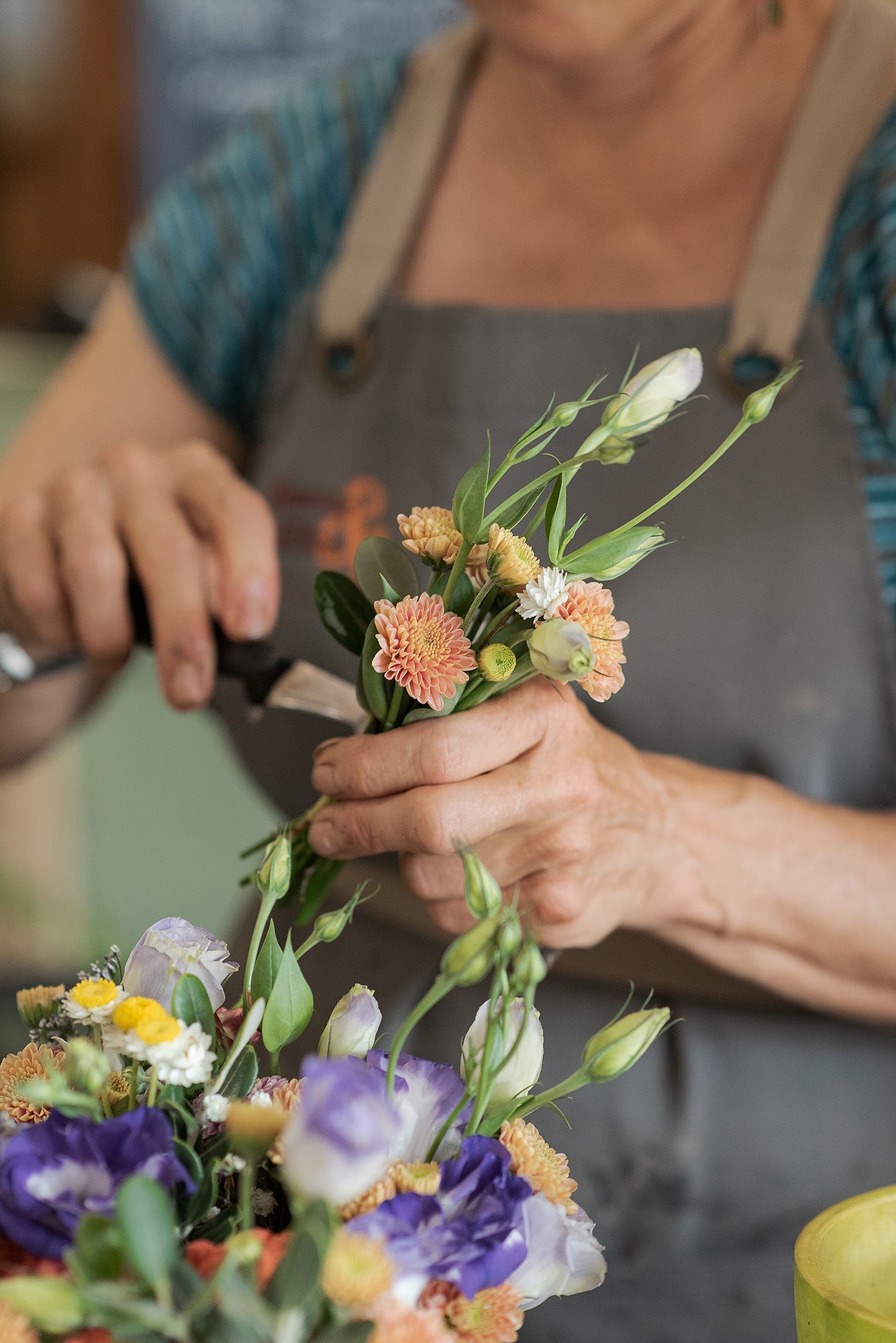 Hands arranging fresh cut flowers including carnations and purple blooms while creating a floral arrangement.