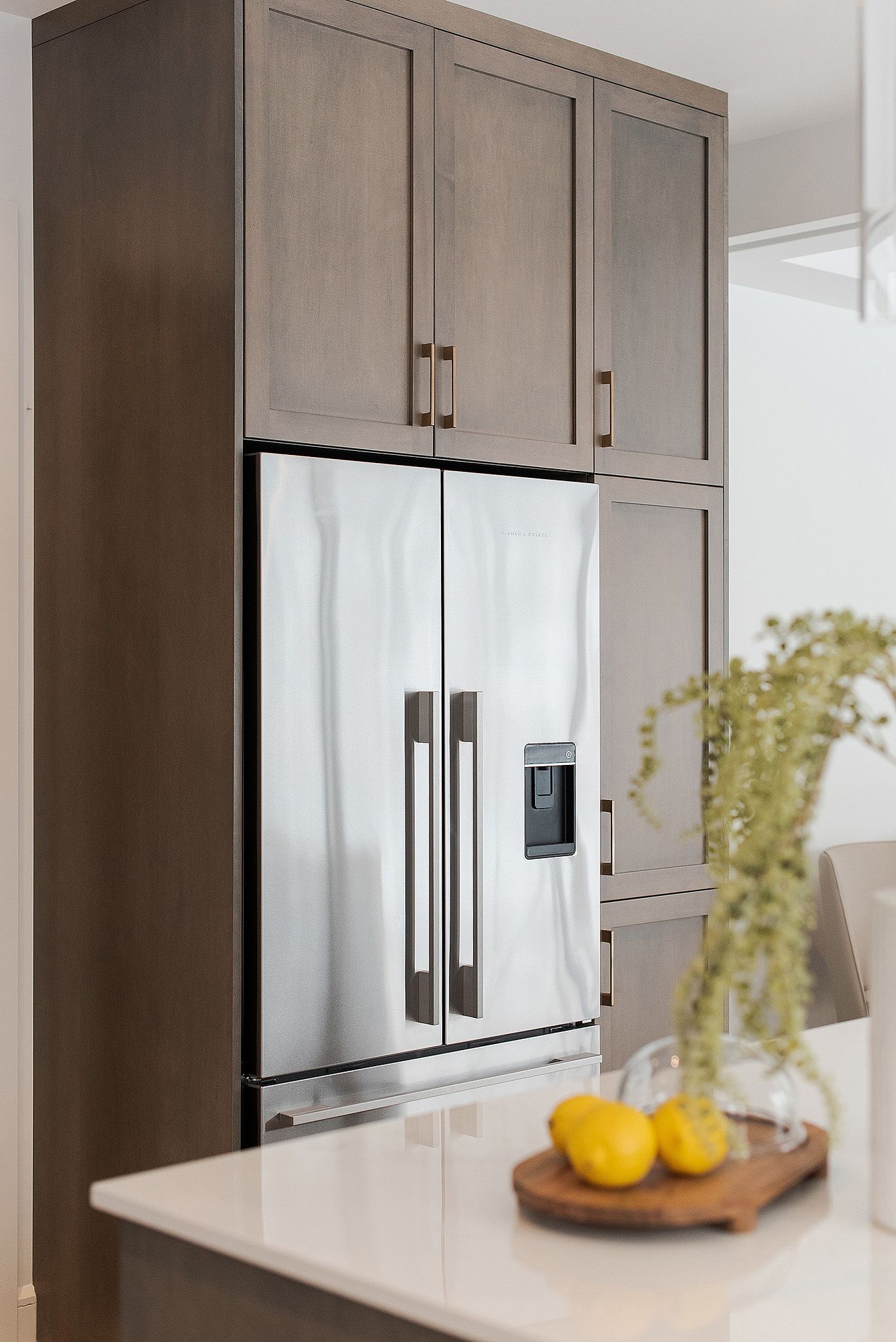 Contemporary kitchen featuring taupe cabinets and stainless steel refrigerators with a wooden cutting board on counter.