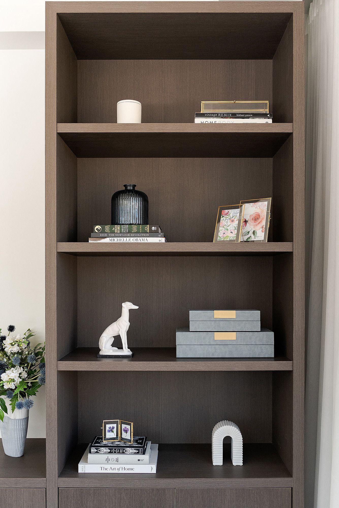 Modern built-in shelving unit with dark gray finish displaying decorative objects, books, and white ceramic sculptures.