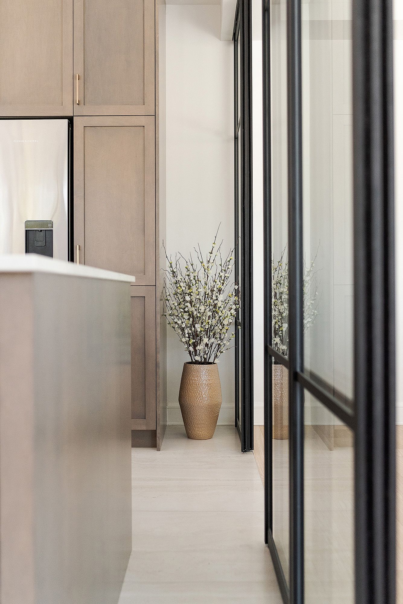 Modern minimalist hallway with glass walls, beige tones, and a ceramic vase with decorative branches.