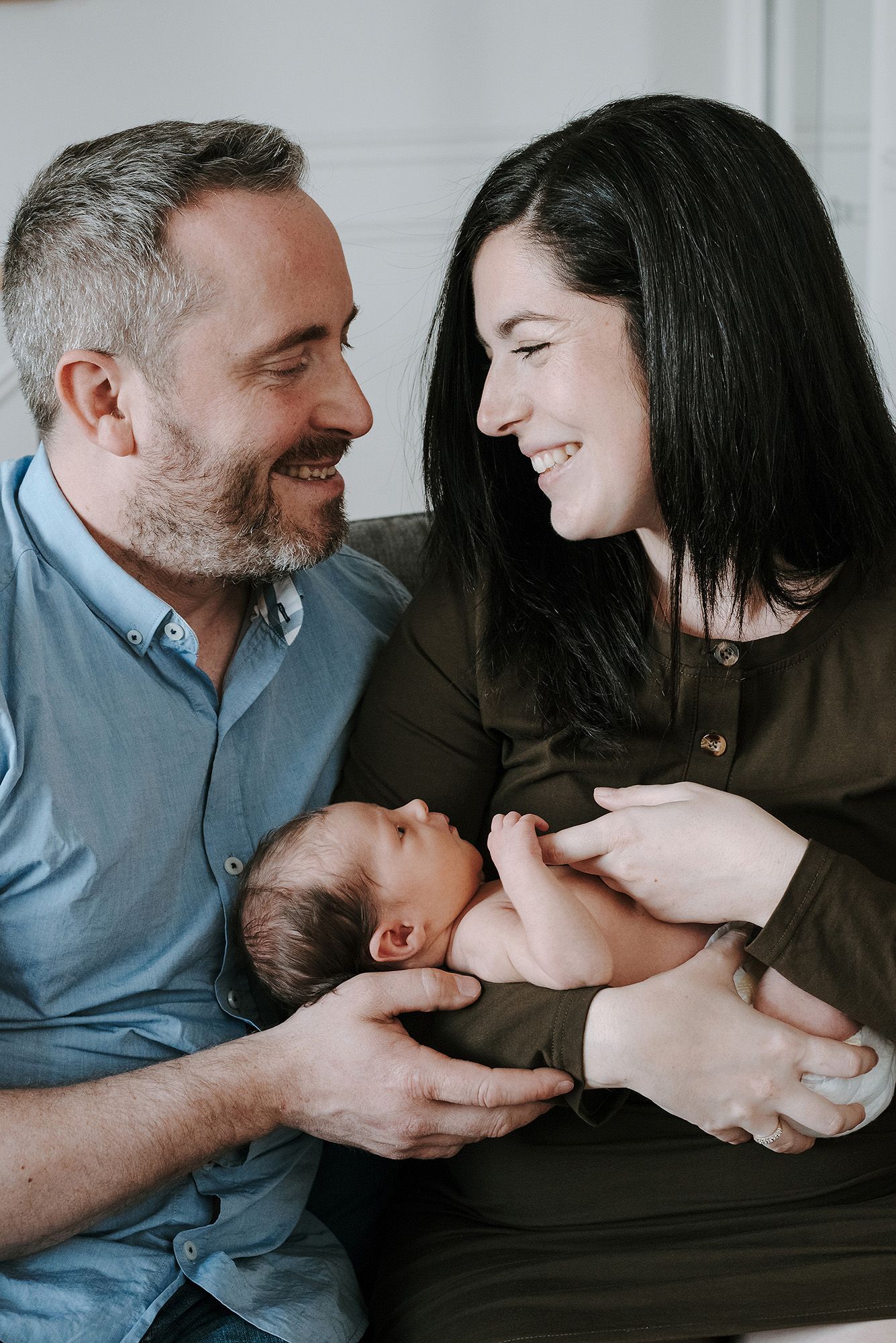 Family bonding with newborn on couch in natural indoor lighting.