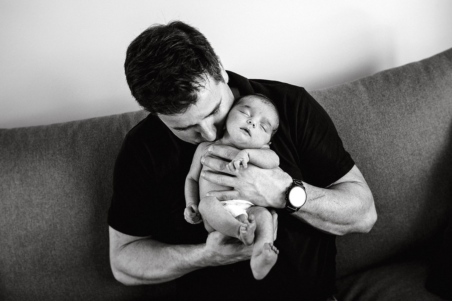Black and white photo of tender moment with sleeping infant on couch.