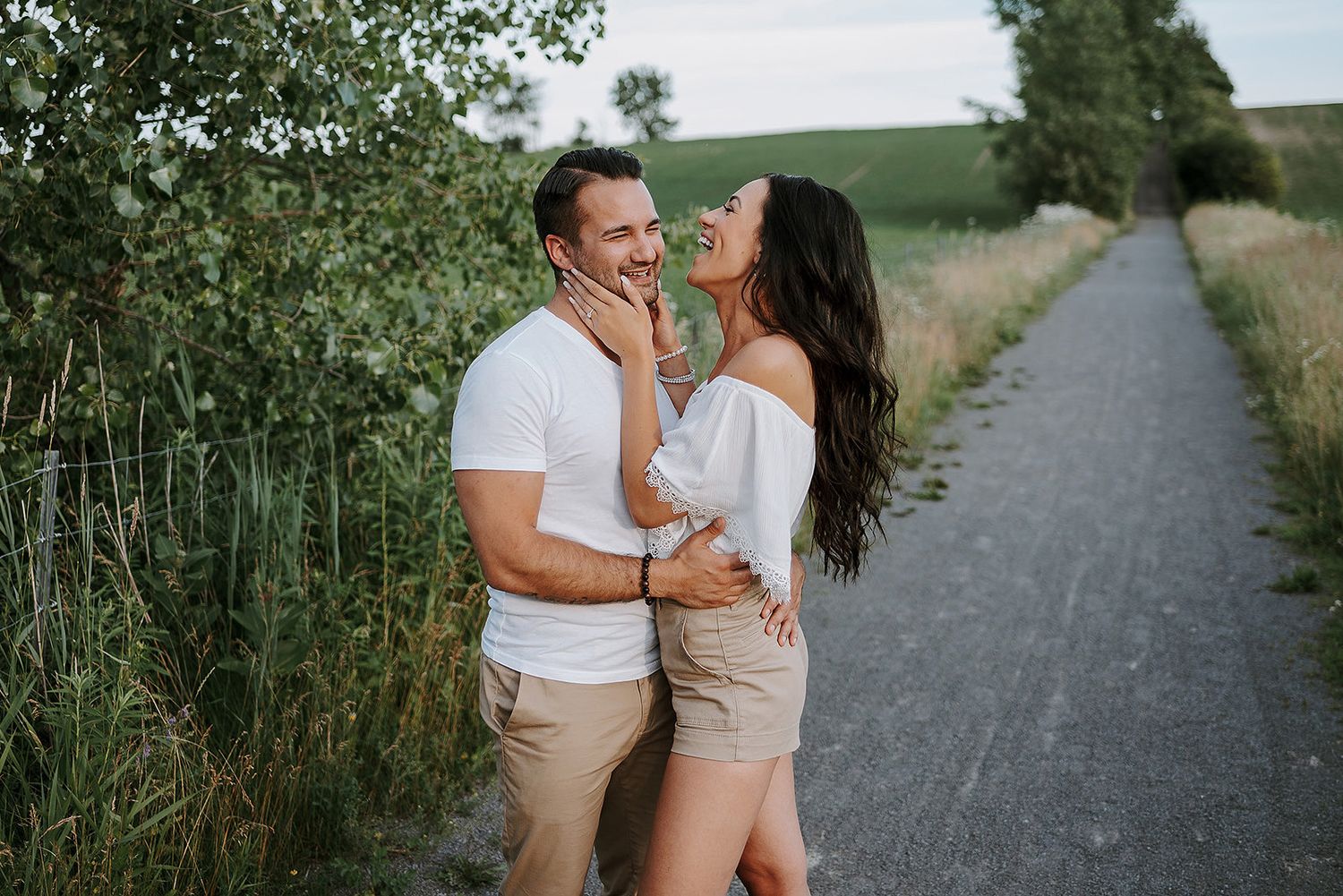 Couple in light summer clothing walking and embracing on a tree-lined path.