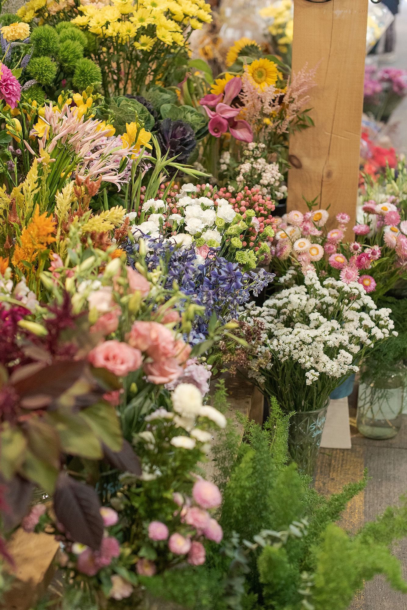 Colorful floral arrangements featuring pink roses, yellow daisies, and white baby's breath displayed in rustic glass vases.