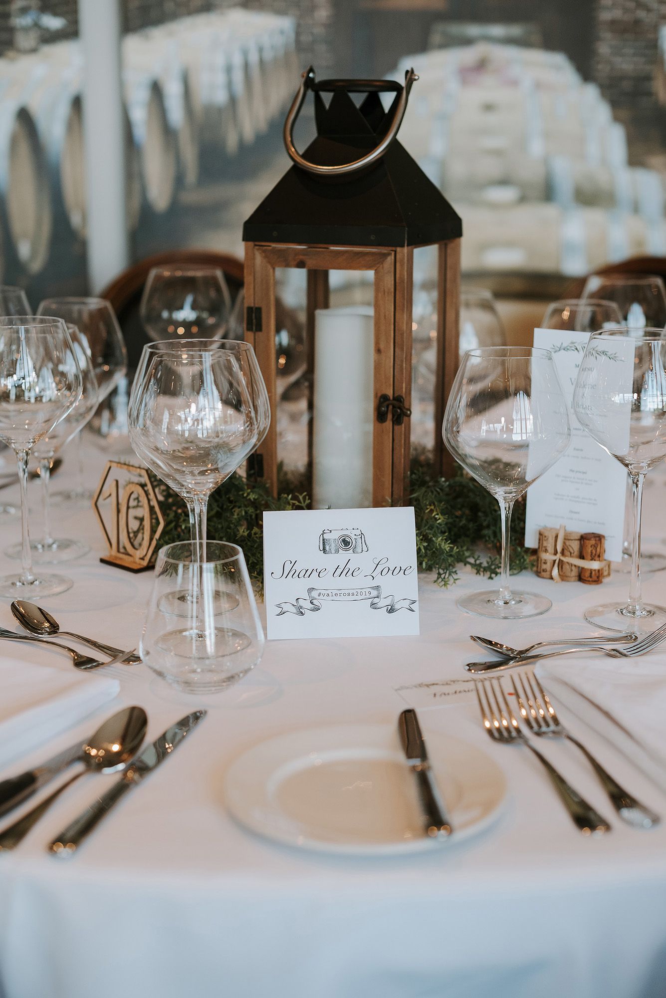 Elegant wedding reception table settings with place cards, wine glasses, and lantern centerpieces on white tablecloths.