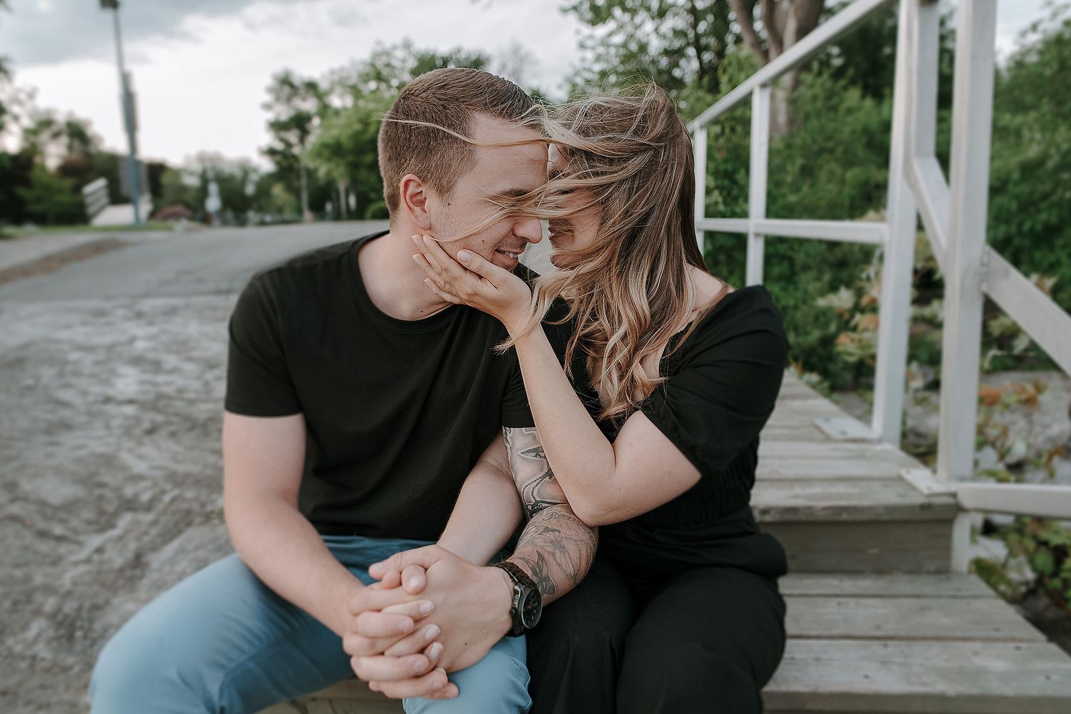 Two people share an intimate moment together on wooden steps surrounded by lush greenery.