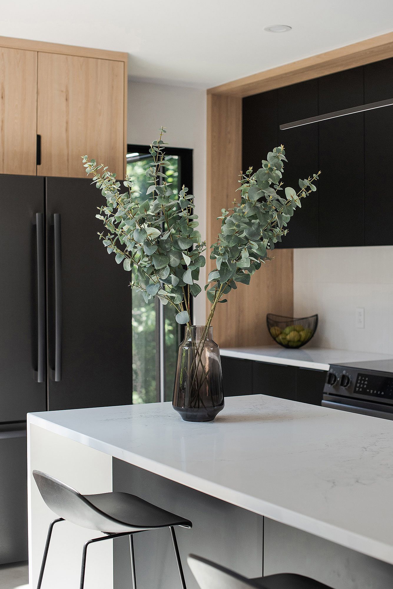 Modern kitchen interior with black and white color scheme featuring wood paneling and eucalyptus plant decor.