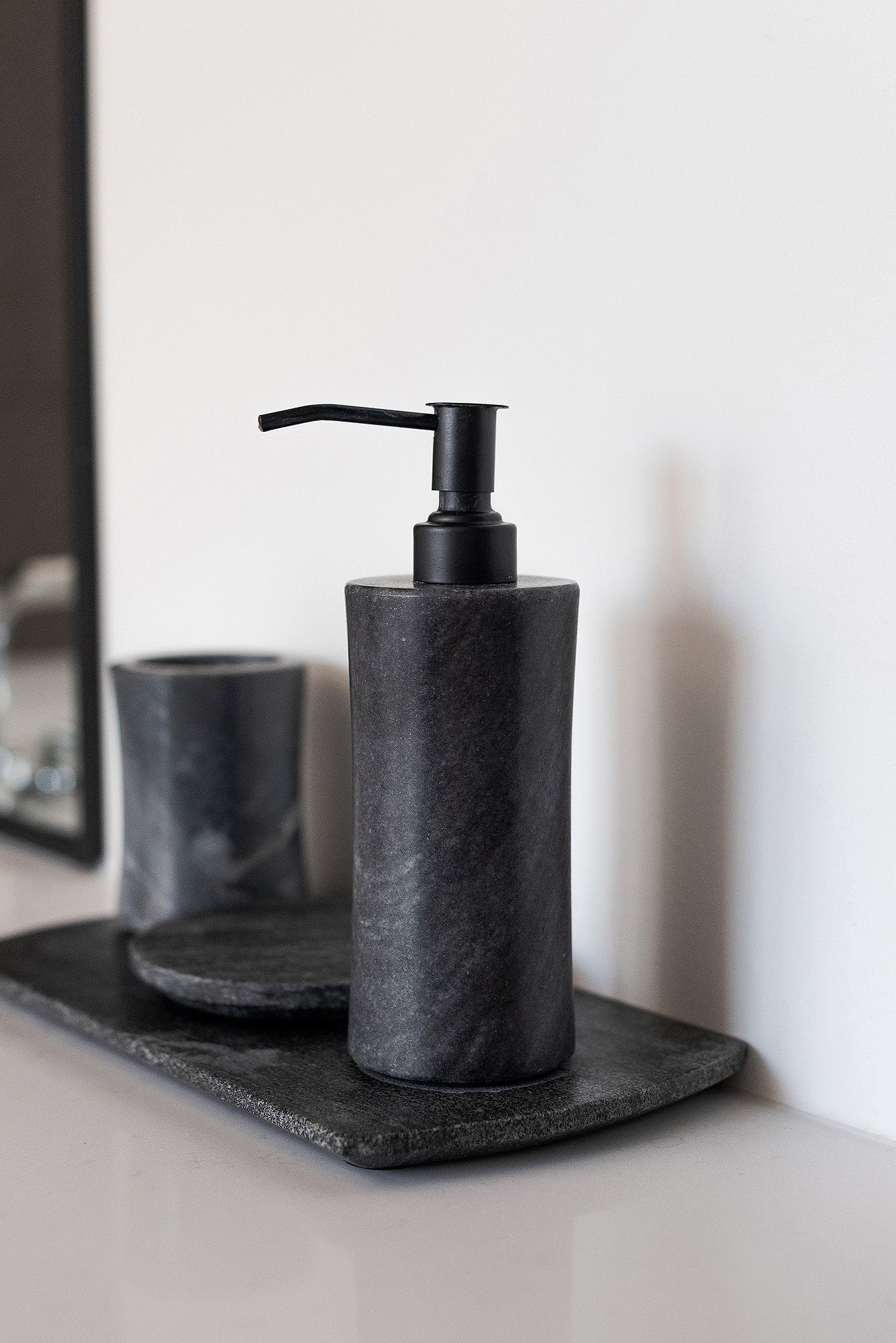 Minimalist black bathroom accessories including soap dispensers and holders arranged on a dark surface against white wall.