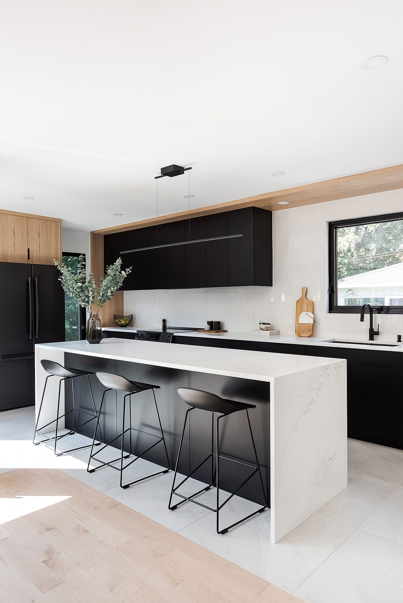 Contemporary white and black kitchen with large island and bar stools in an open-concept space.