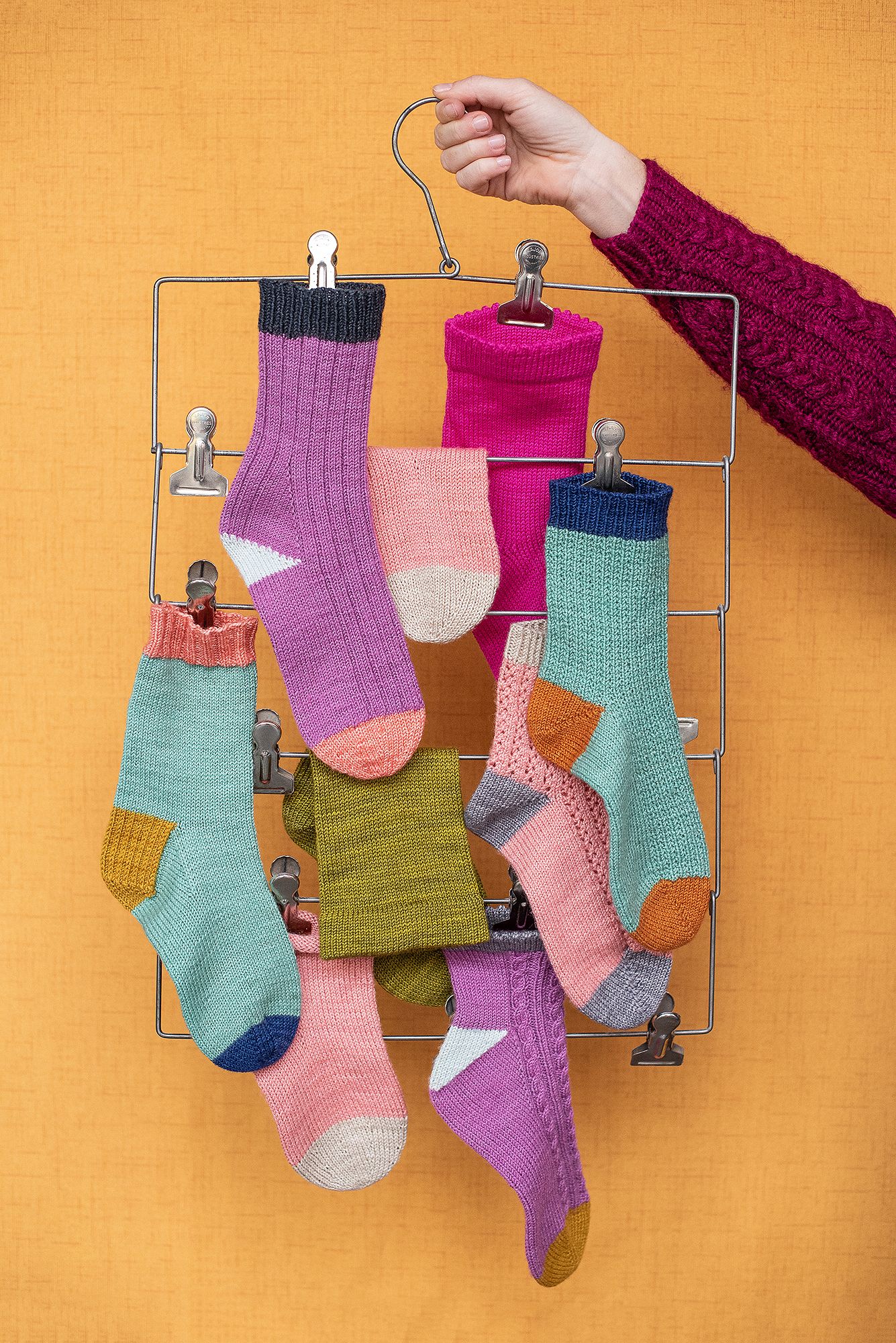 Colorful handmade socks hanging on a drying rack against yellow background.