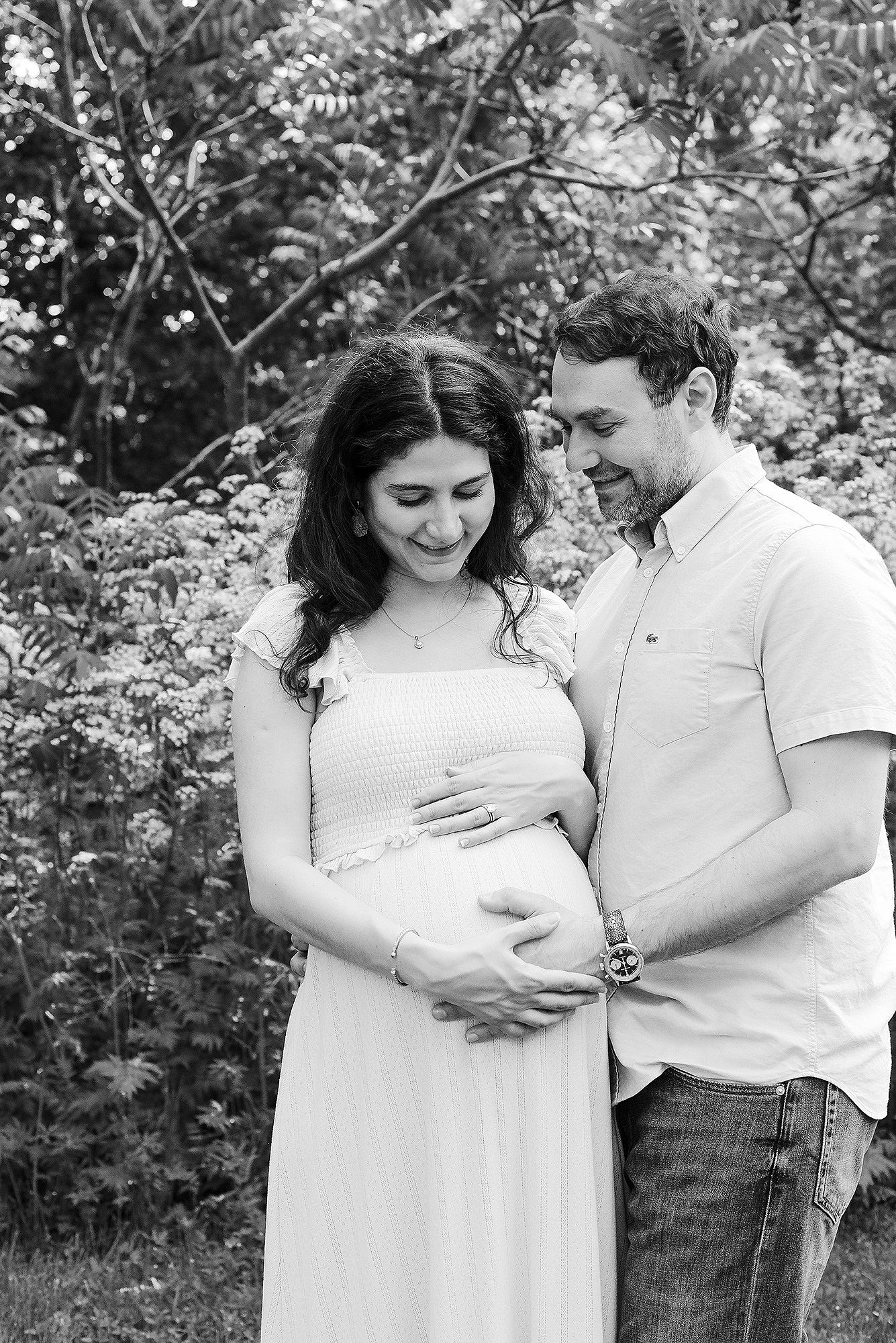 A couple in white and casual attire share tender moments outdoors in a series of black and white photographs.