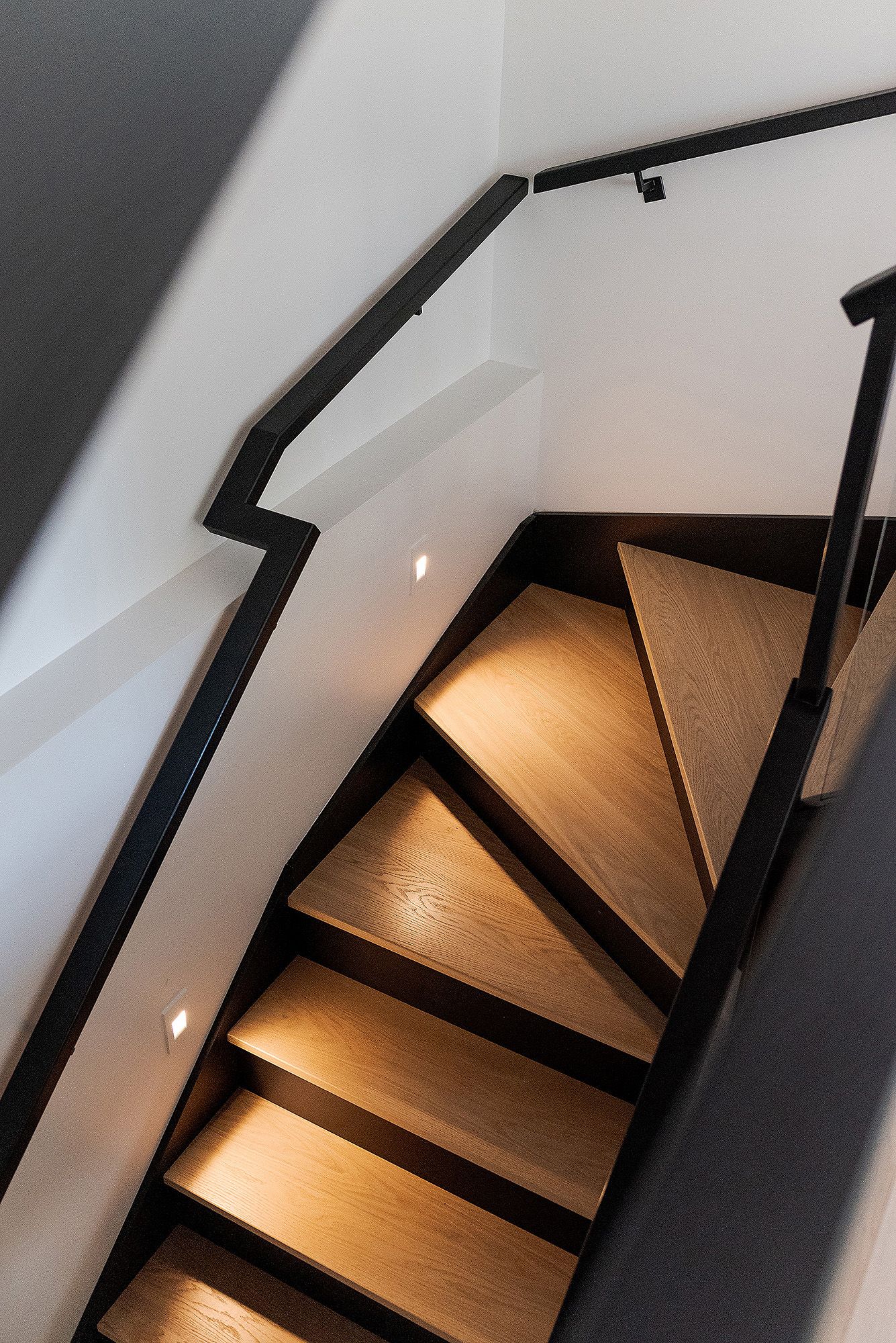 Close-up of wooden staircase with black railings and built-in LED lighting illuminating each step.