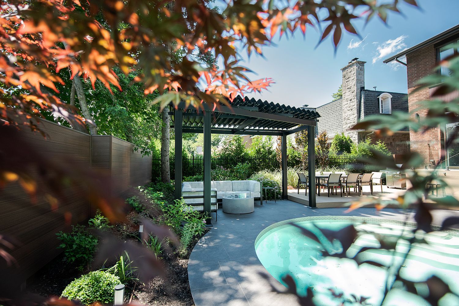 Japanese maple leaves frame a tranquil outdoor patio with turquoise cushioned seating and wooden pergola.