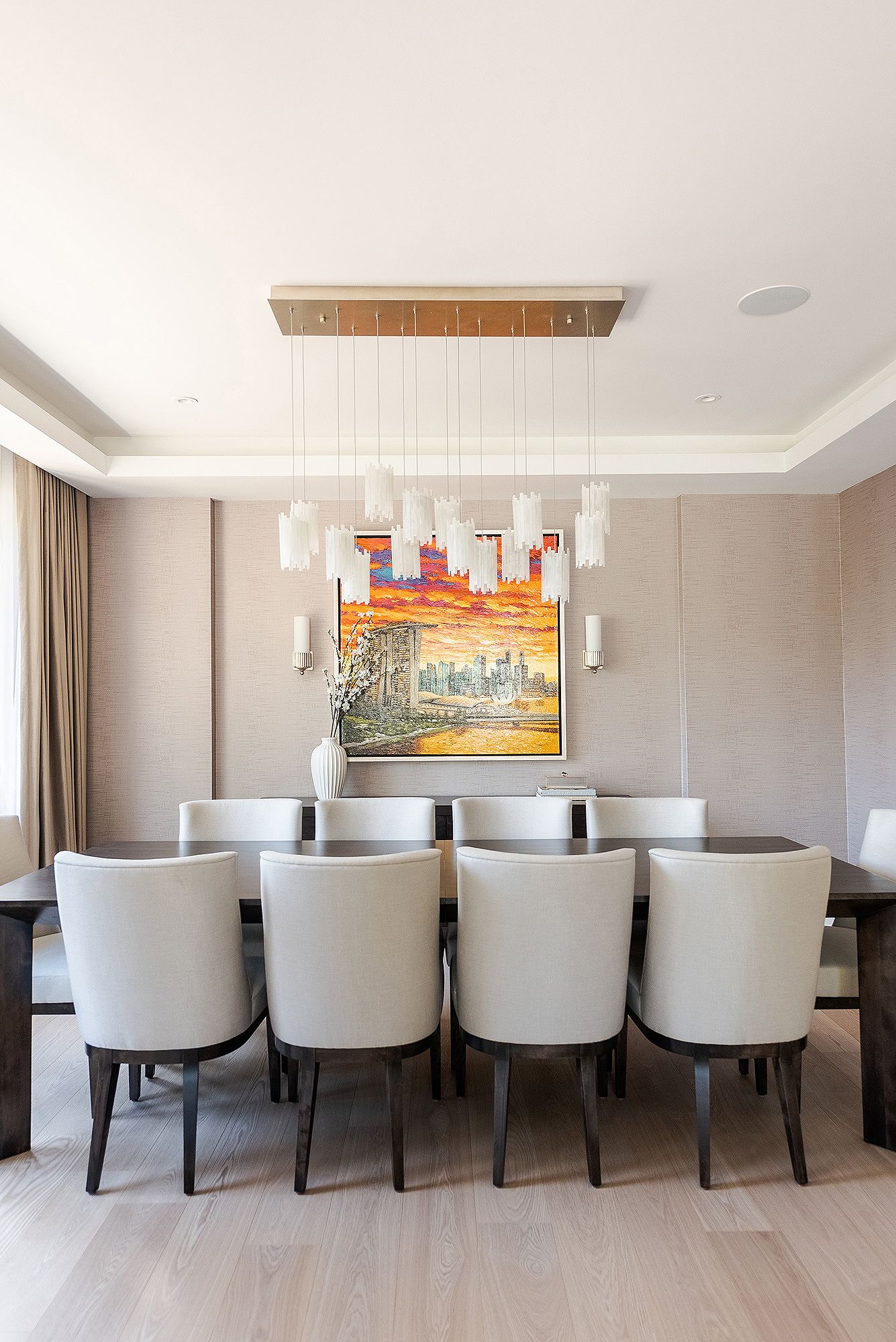 Modern dining room with white upholstered chairs, pendant lights, and colorful cityscape artwork above dark wood table.