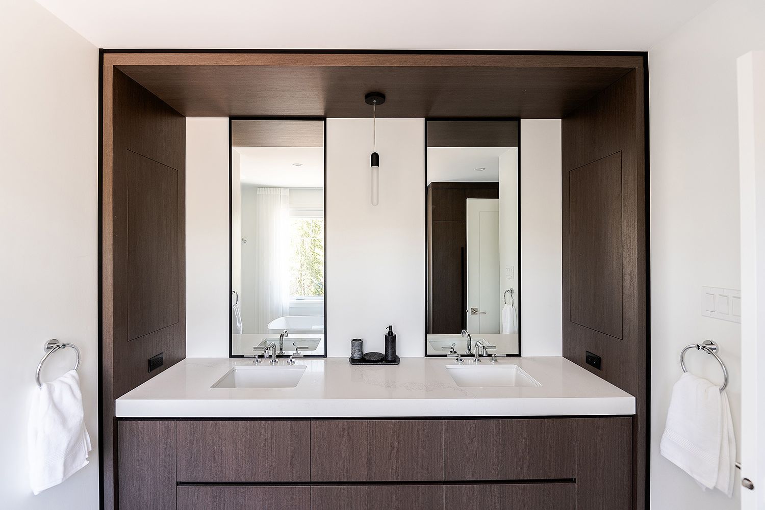 Modern bathroom interior with dark wood cabinets, white countertops and sleek minimalist design elements.