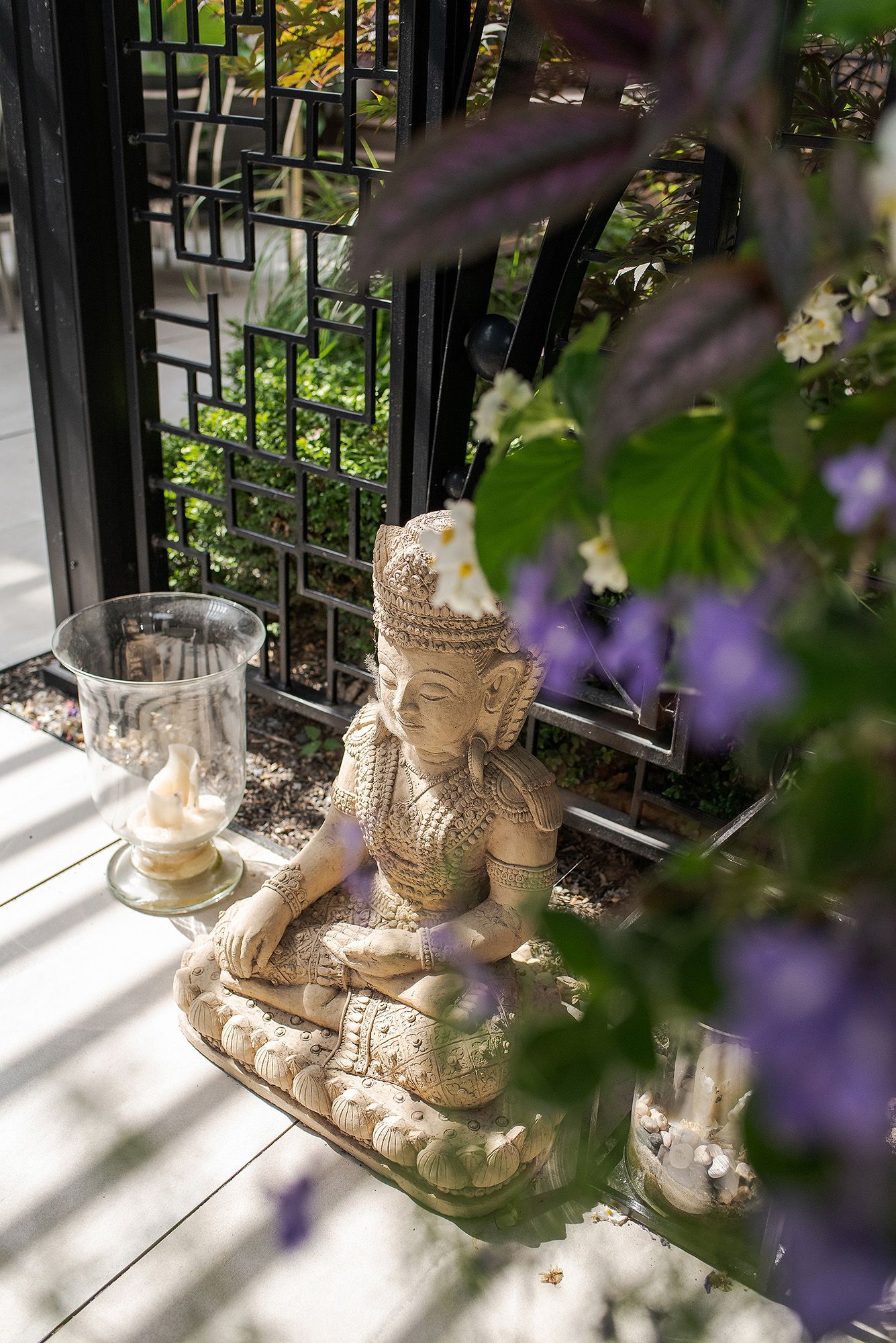 Buddha statues arranged on a windowsill with purple flowers in the foreground create a peaceful garden atmosphere.