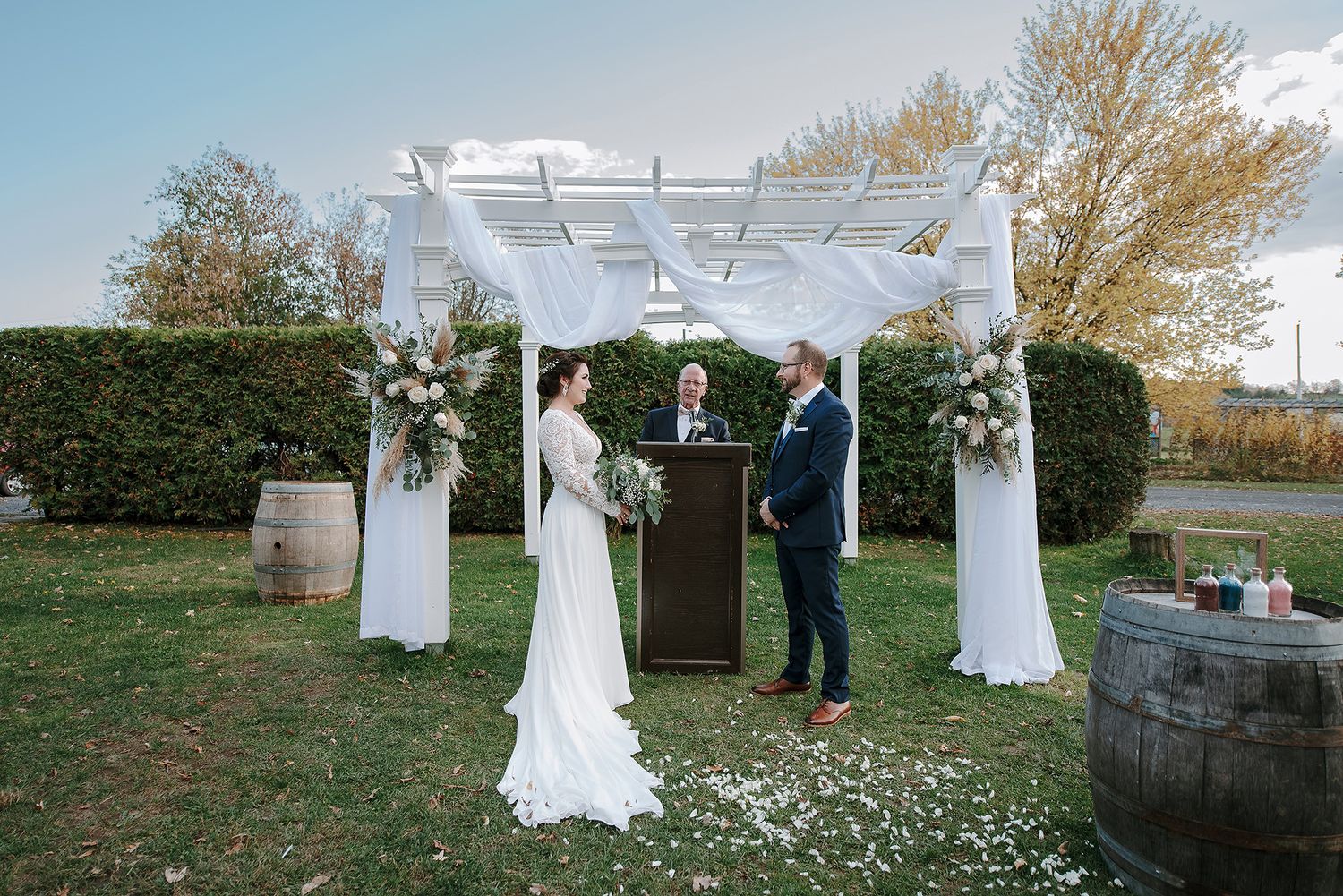 A series of outdoor wedding ceremony photos showing a white arbor decorated with floral arrangements in a rustic setting.