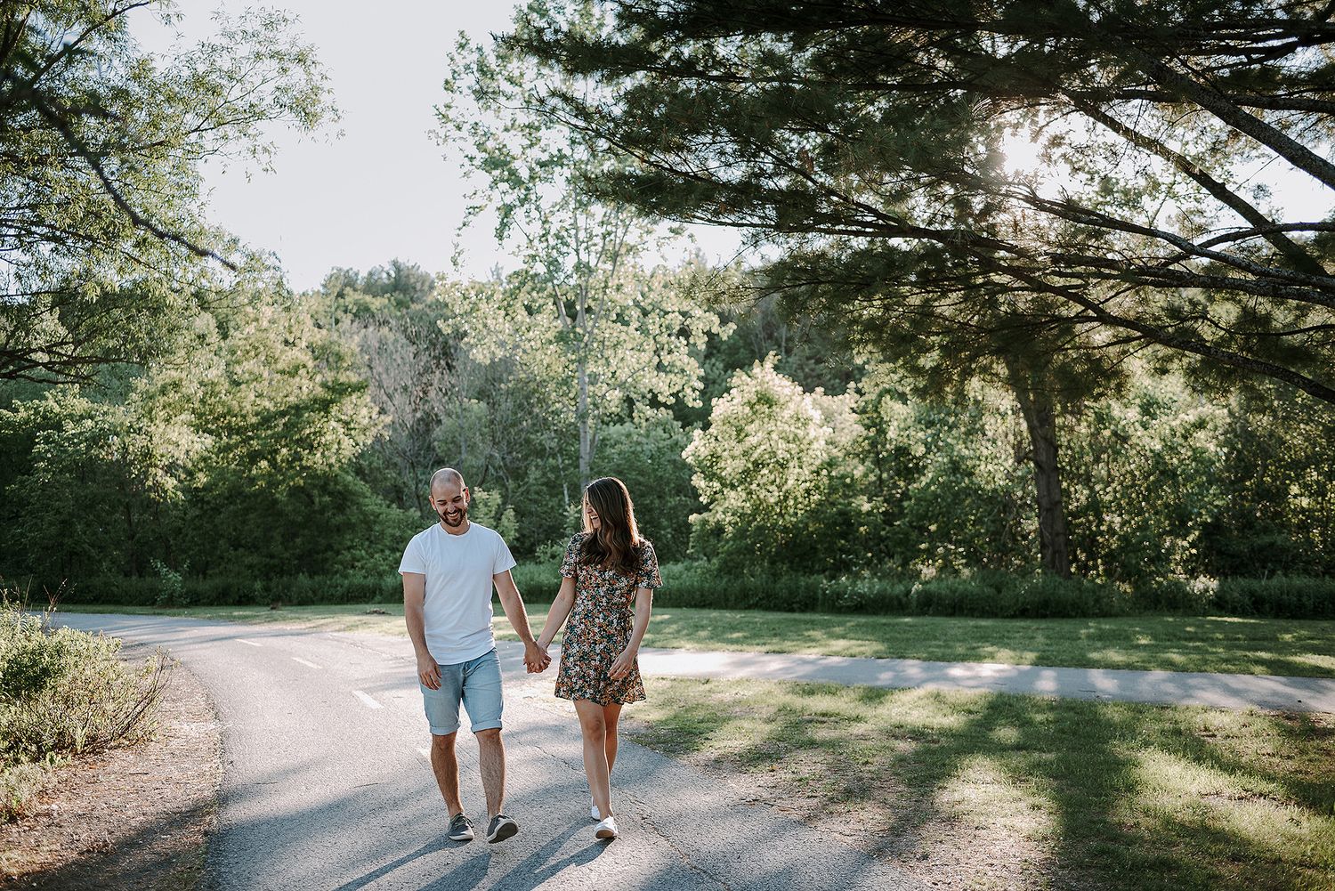 Couple walking hand in hand along a tree-lined path during golden hour.