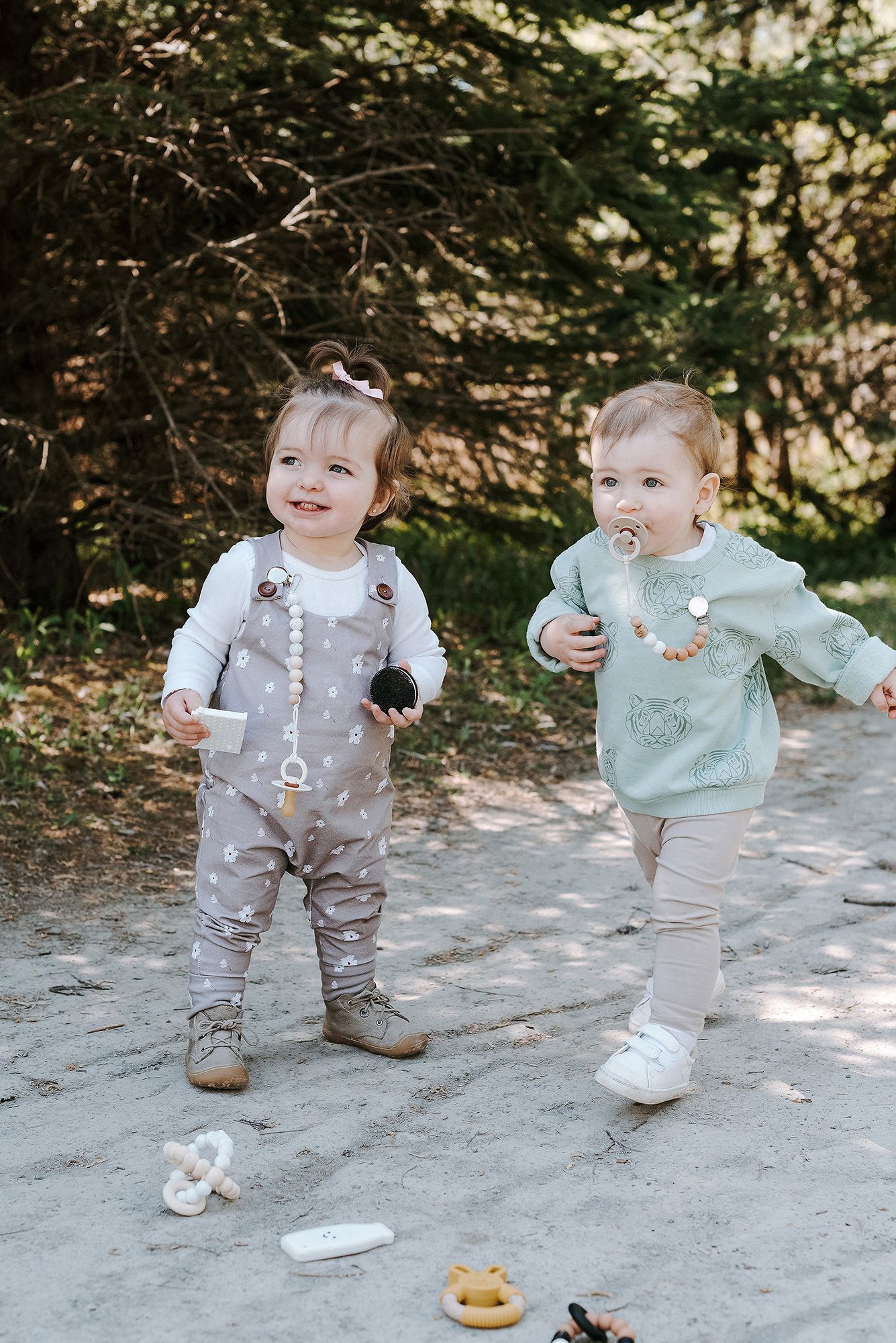 Two toddlers in matching gray outfits playing together on a path outdoors.