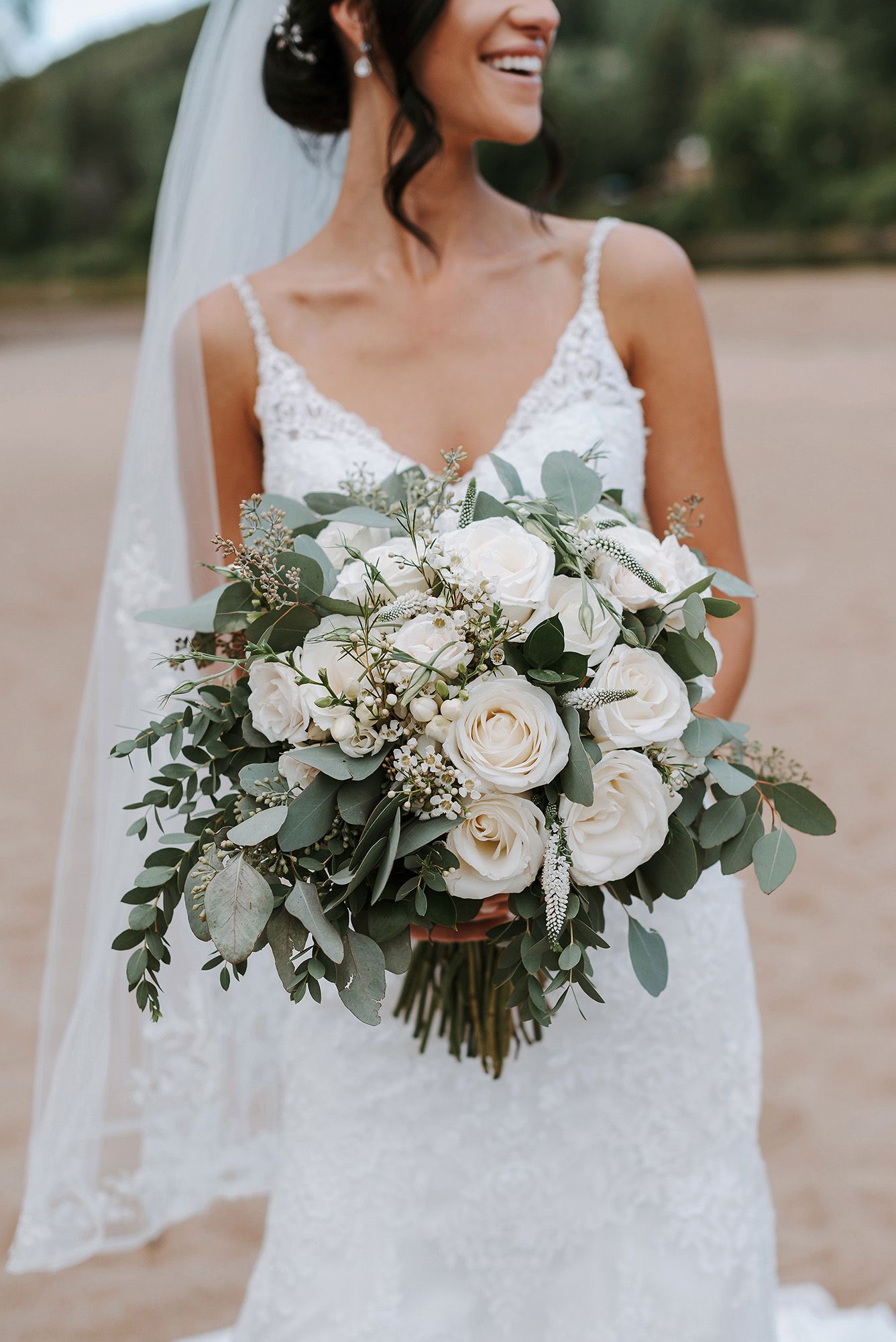 A beautiful bridal bouquet with white roses, eucalyptus leaves and baby's breath against a white lace wedding dress.