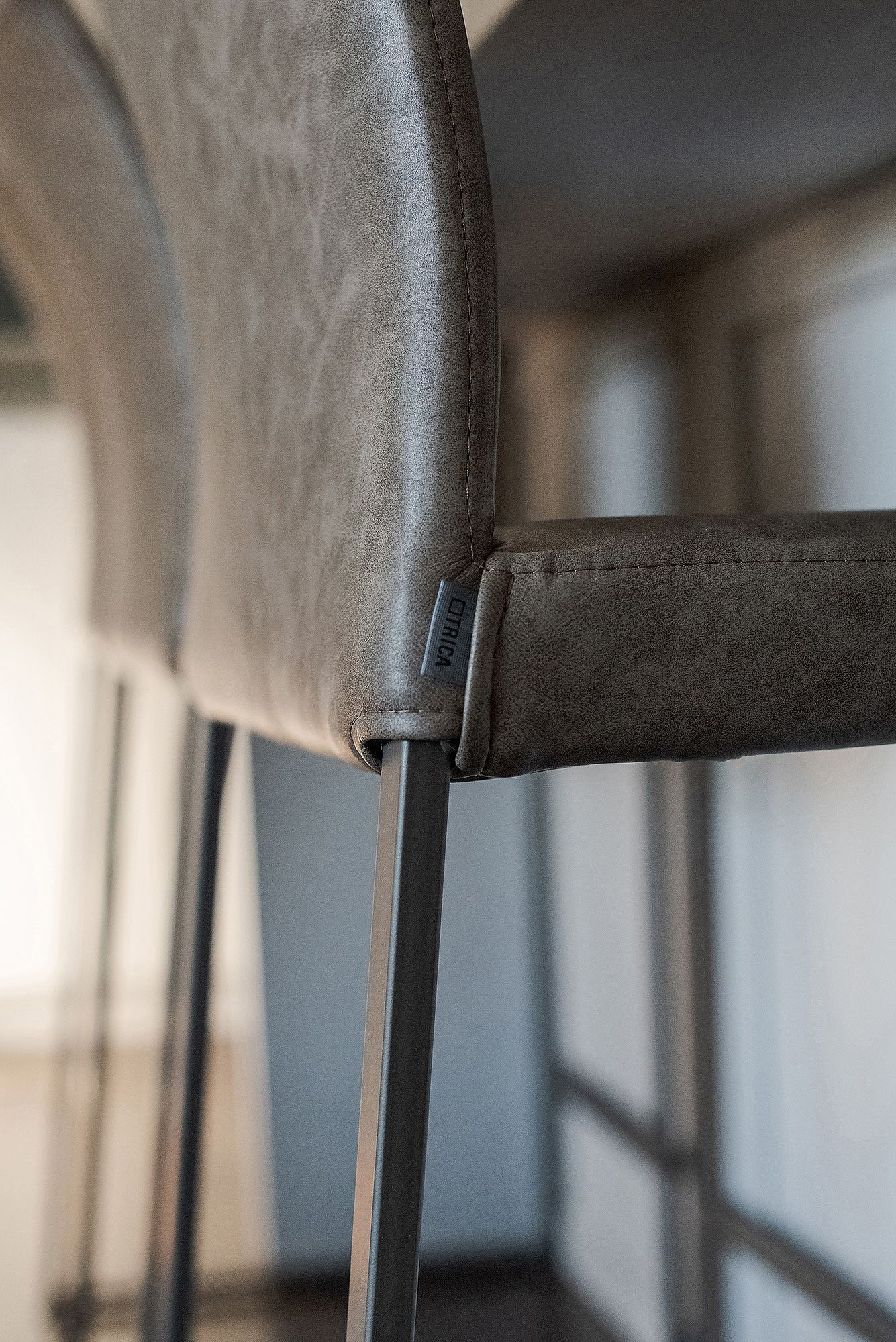 Close-up detail of a modern grey upholstered dining chair showing the curved backrest and metal frame.