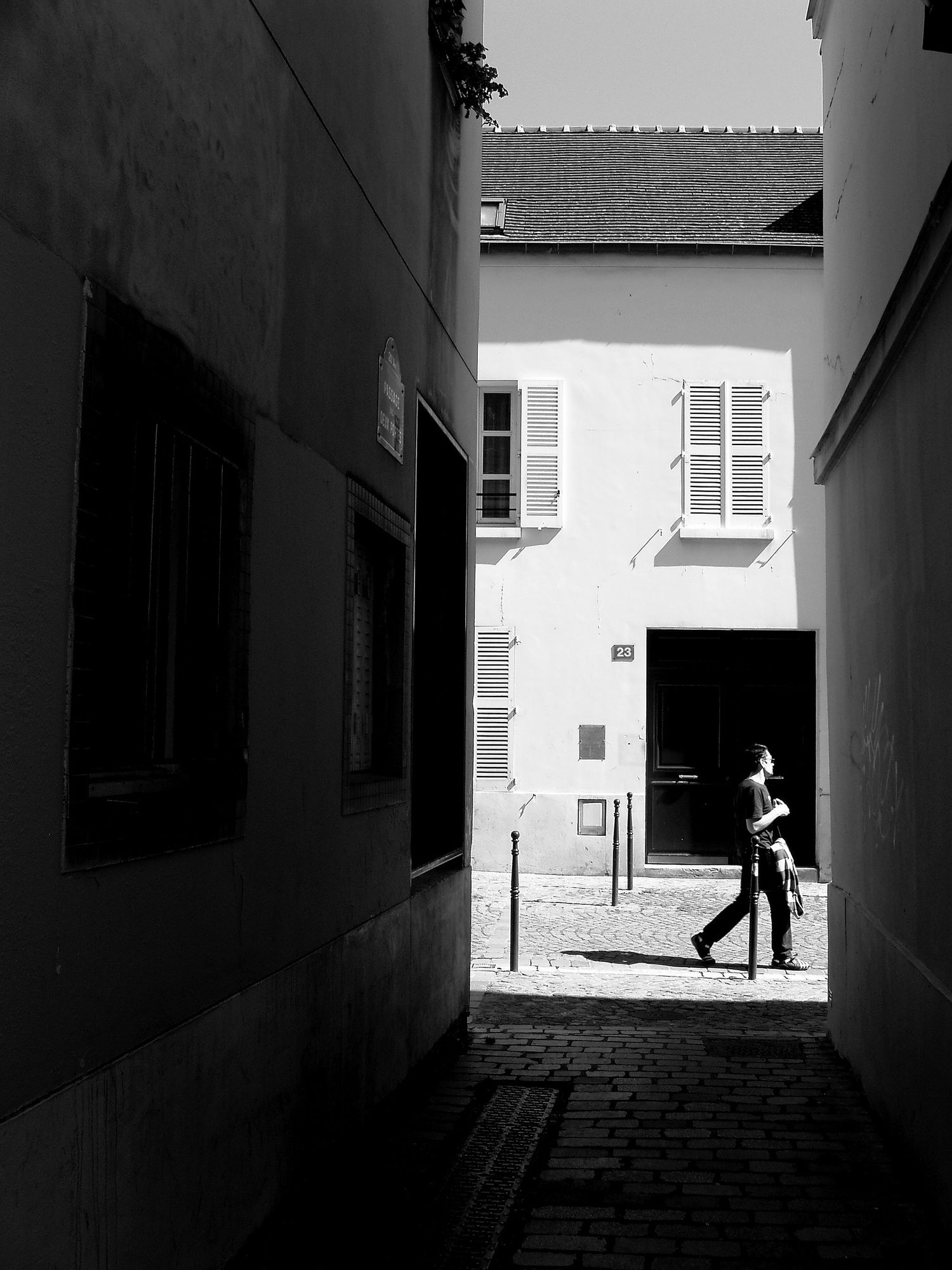 Narrow alleyway leading to white building with dark doorway in black and white.
