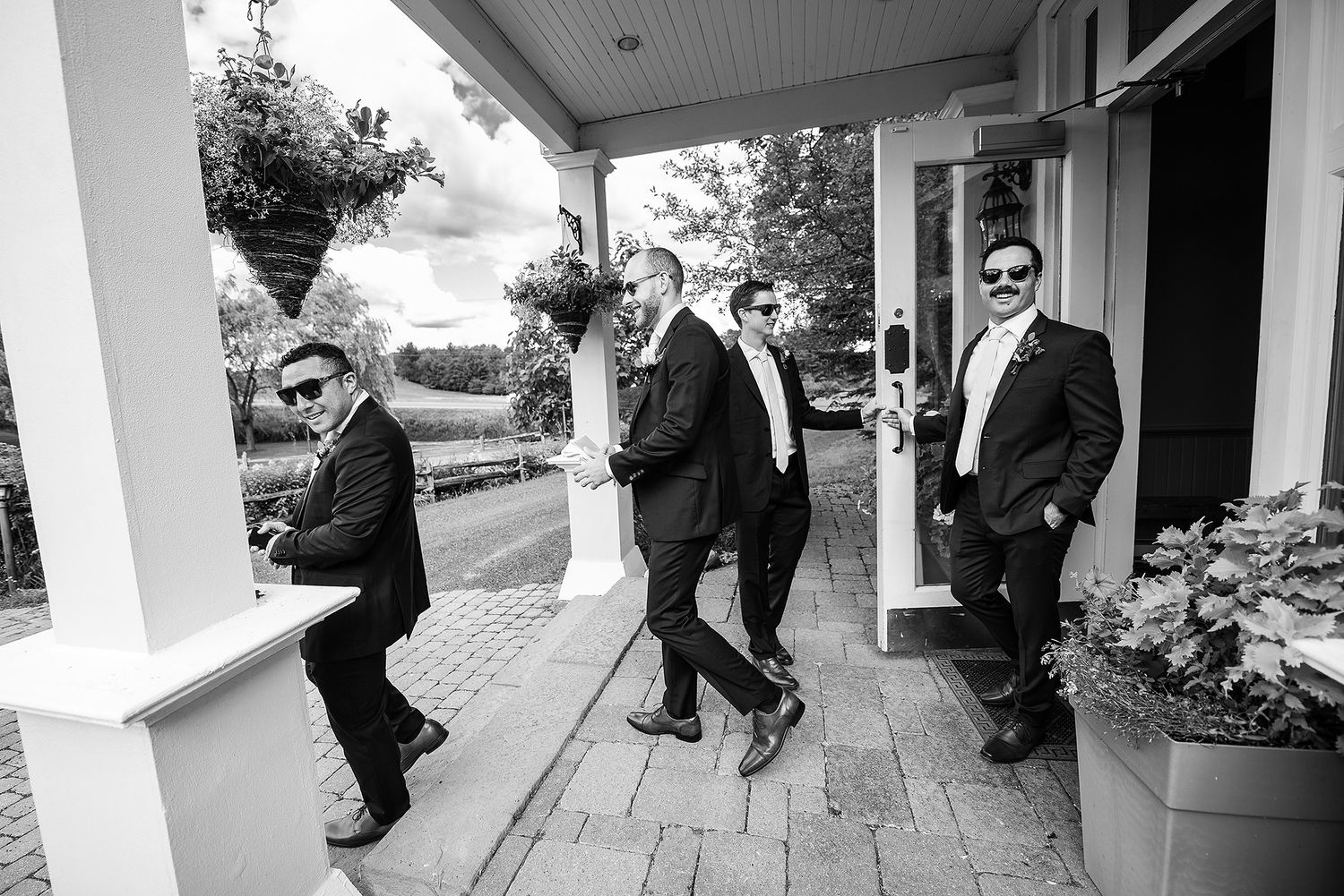 Wedding party members walk along a covered porch of an elegant building.