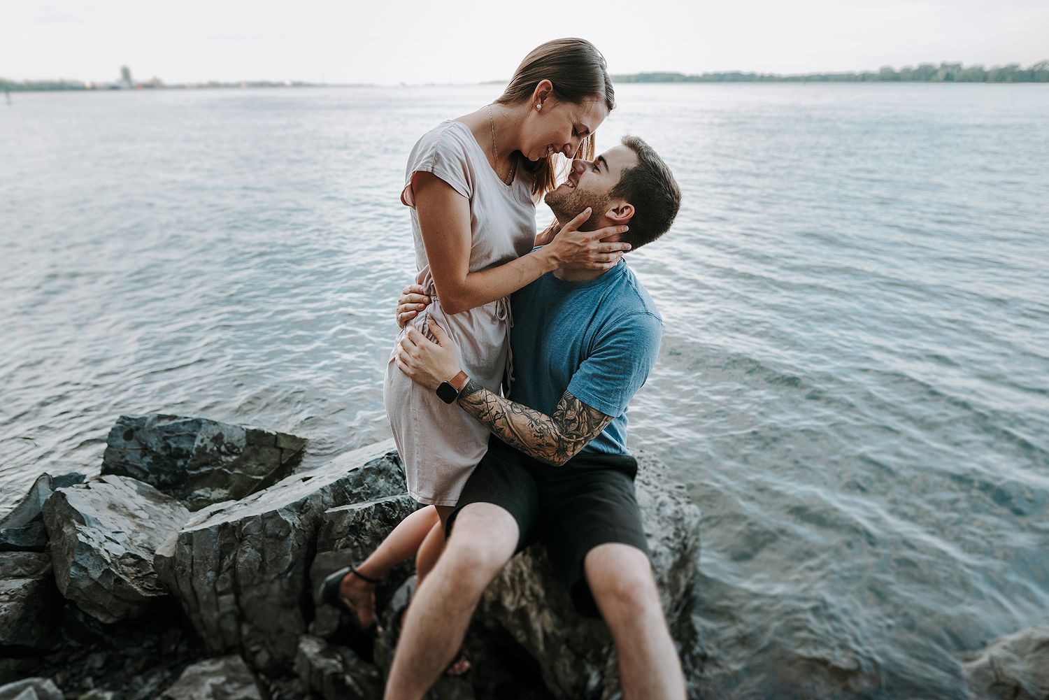 Romantic couple poses on rocky shoreline with water view at sunset.